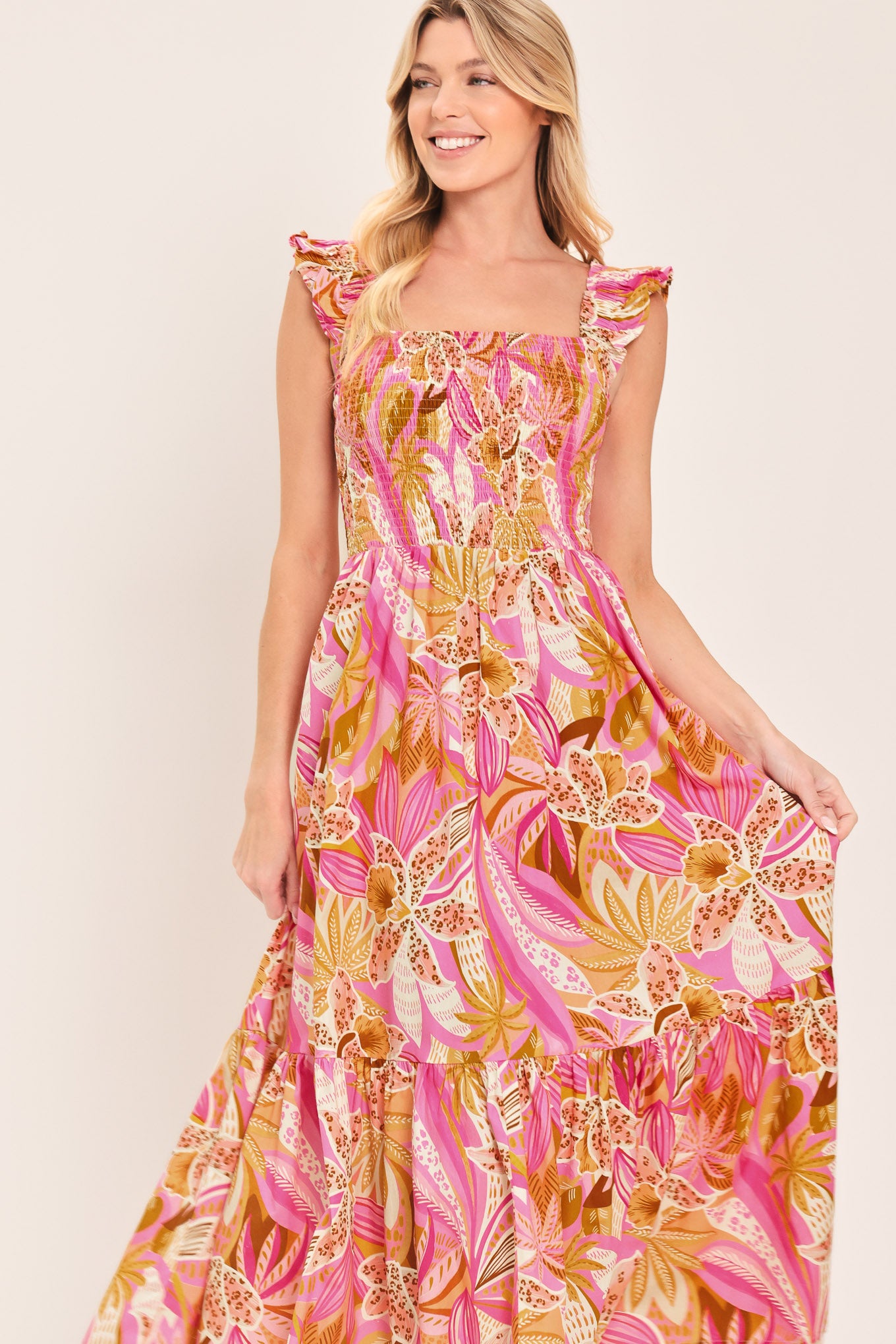 Woman wearing a pink tropical floral midi dress featuring square neckline, ruffle sleeve, smocked bodice and tier skirt | Flying Tomato