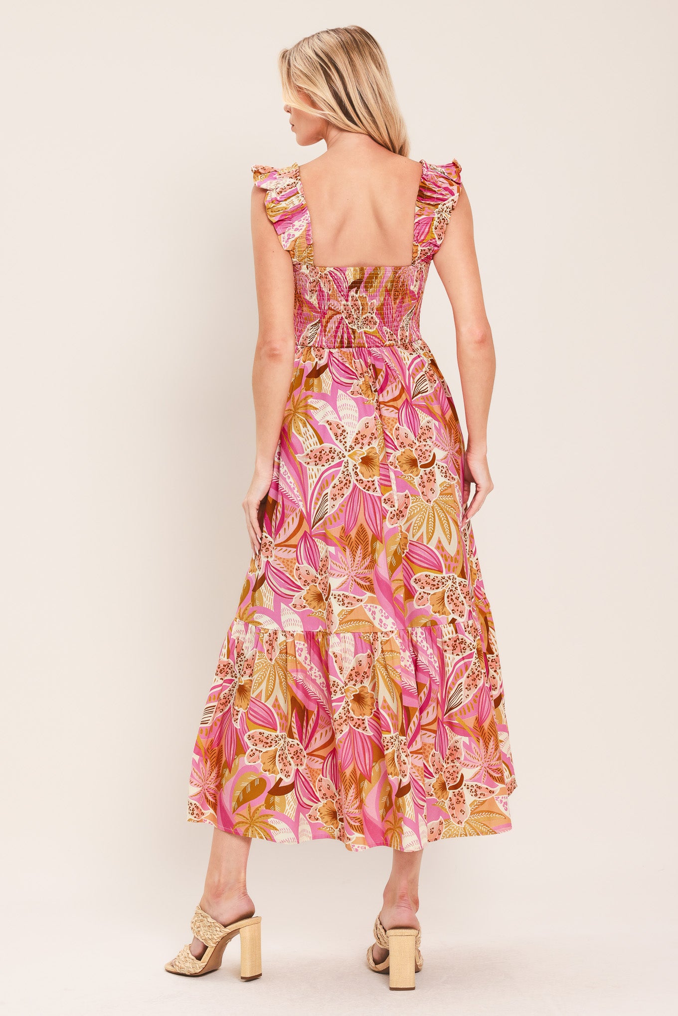 Woman wearing a pink tropical floral midi dress featuring square neckline, ruffle sleeve, smocked bodice and tier skirt | Flying Tomato
