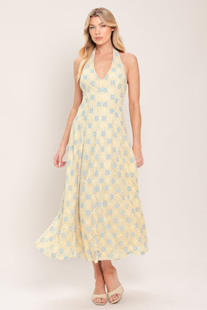 Woman wearing a yellow with blue floral lace midi dress featuring halter neckline, full circle skirt and back zipper closure with back neck tie | Flying Tomato