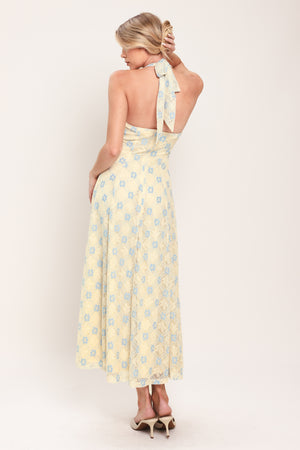Woman wearing a yellow with blue floral lace midi dress featuring halter neckline, full circle skirt and back zipper closure with back neck tie | Flying Tomato