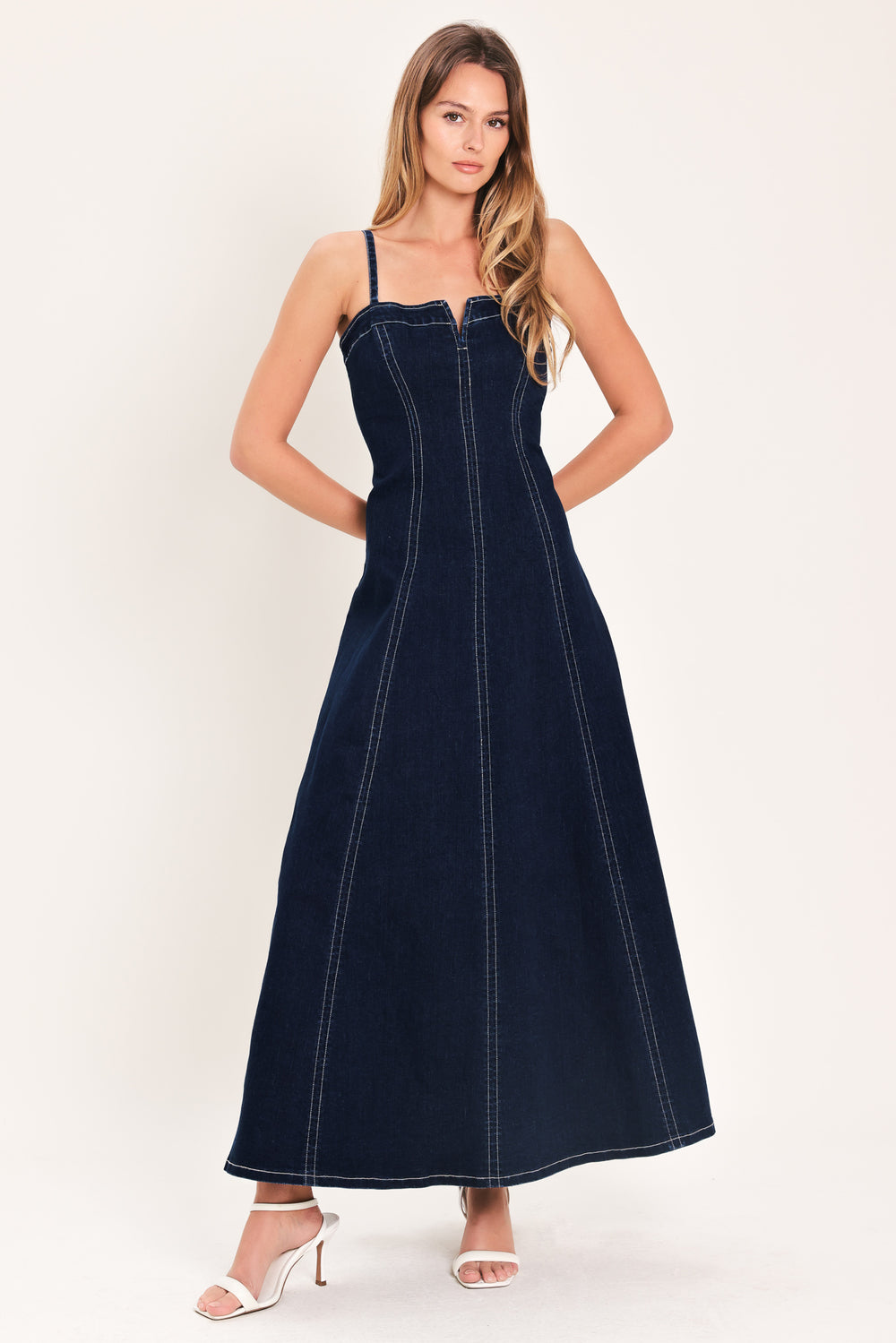 Woman wearing a dark indigo denim midi dress featuring straight neckline with V cut out, straps, circle skirt and back zipper closure | Flying Tomato