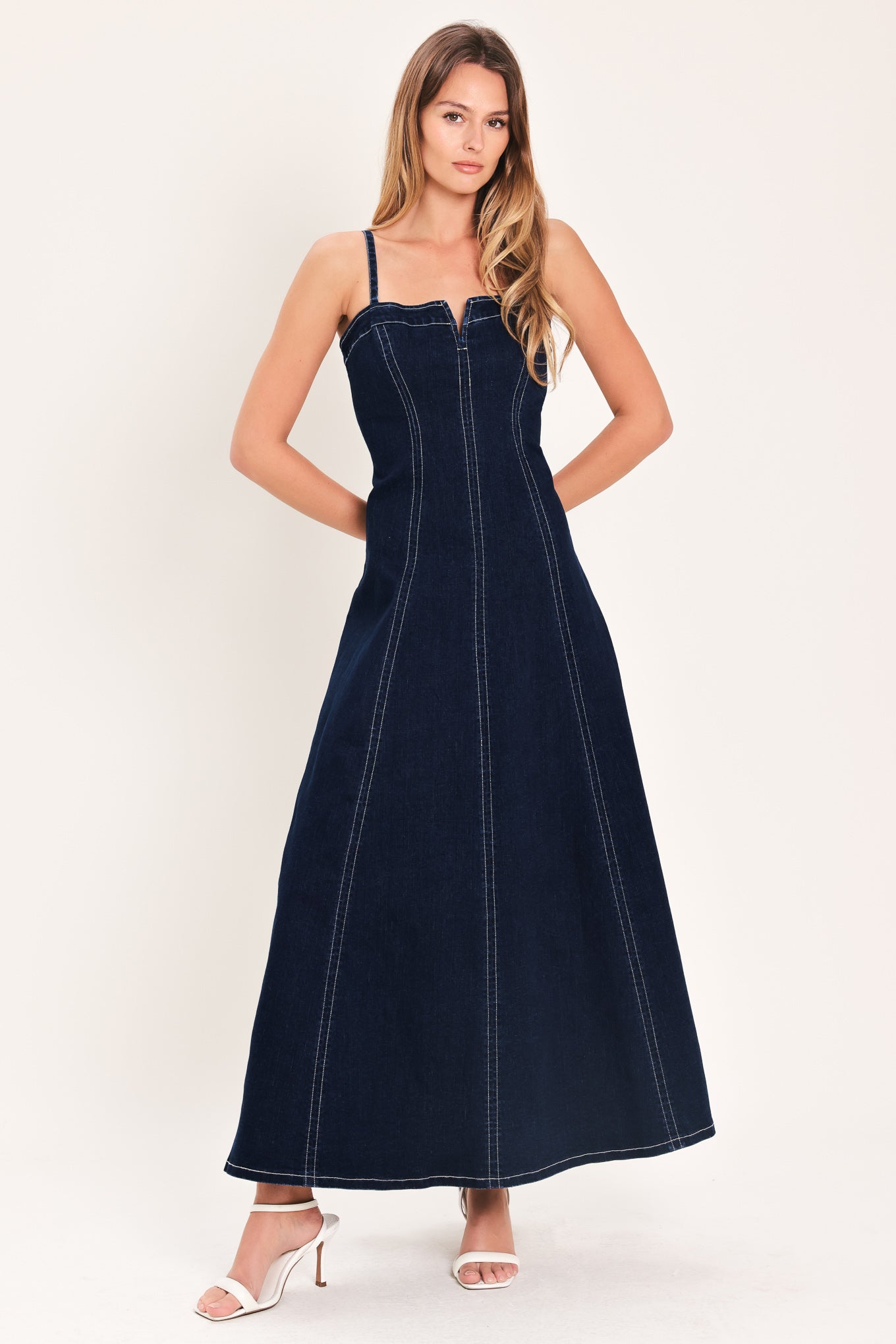 Woman wearing a dark indigo denim midi dress featuring straight neckline with V cut out, straps, circle skirt and back zipper closure | Flying Tomato