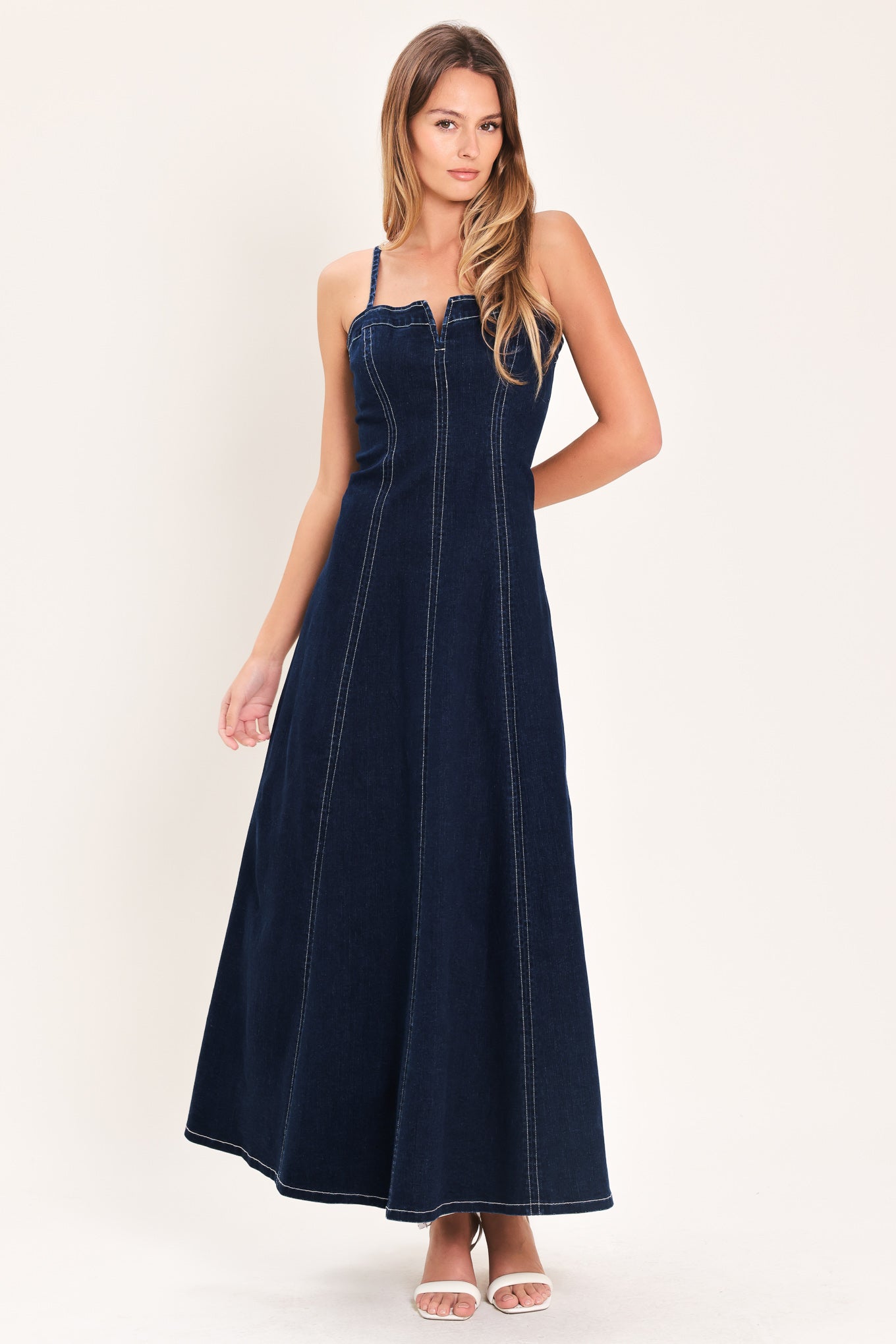 Woman wearing a dark indigo denim midi dress featuring straight neckline with V cut out, straps, circle skirt and back zipper closure | Flying Tomato