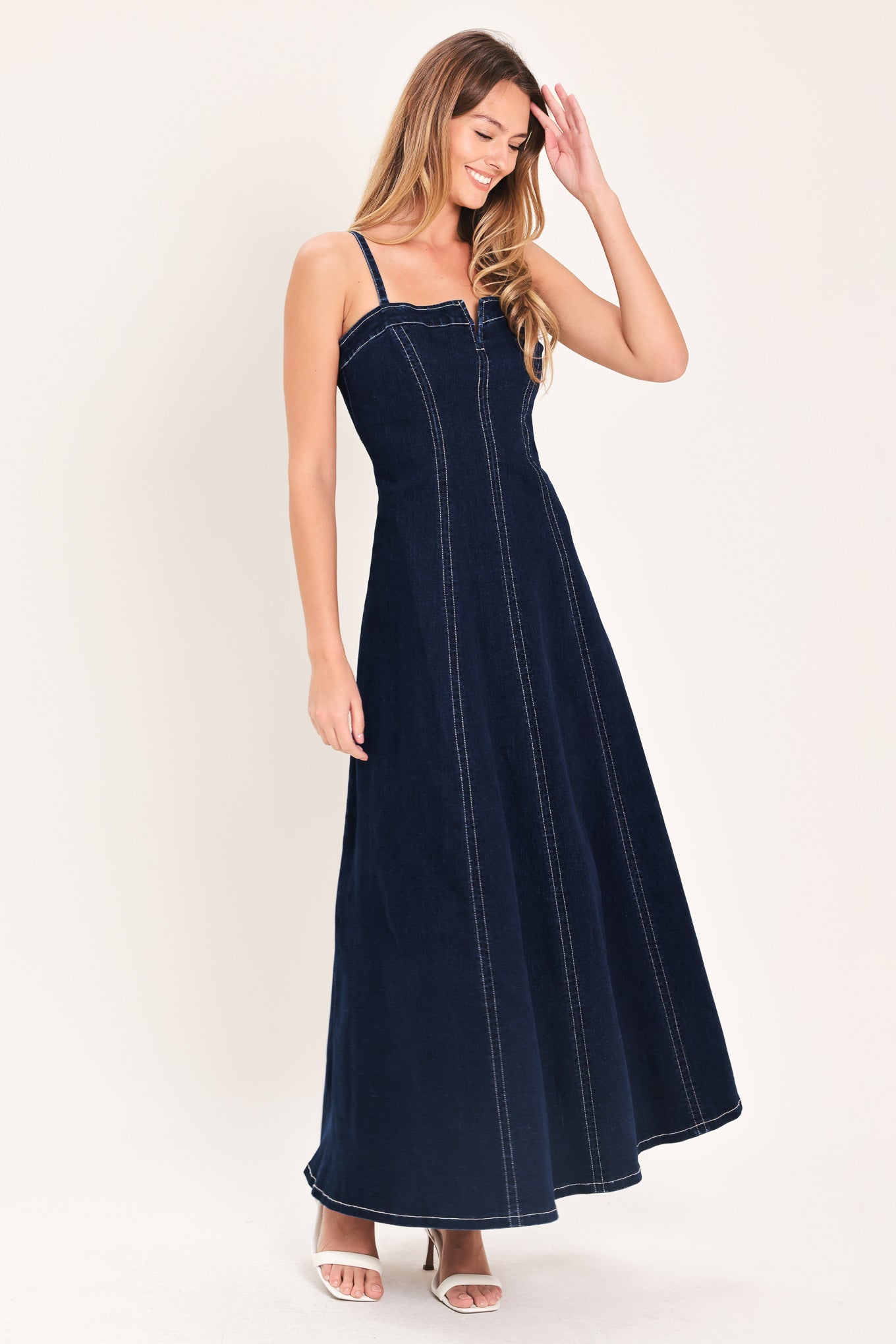 Woman wearing a dark indigo denim midi dress featuring straight neckline with V cut out, straps, circle skirt and back zipper closure | Flying Tomato