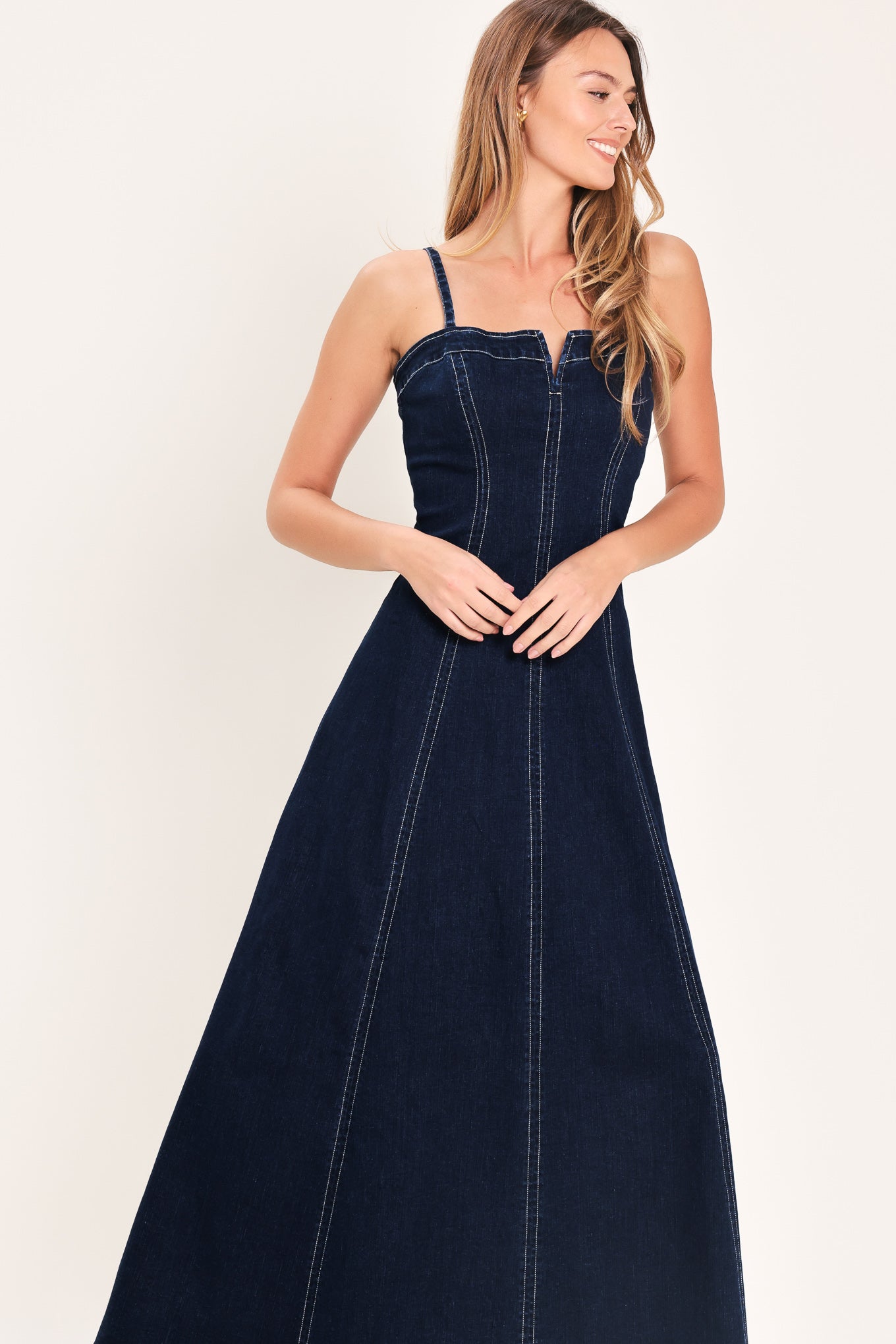 Woman wearing a dark indigo denim midi dress featuring straight neckline with V cut out, straps, circle skirt and back zipper closure | Flying Tomato