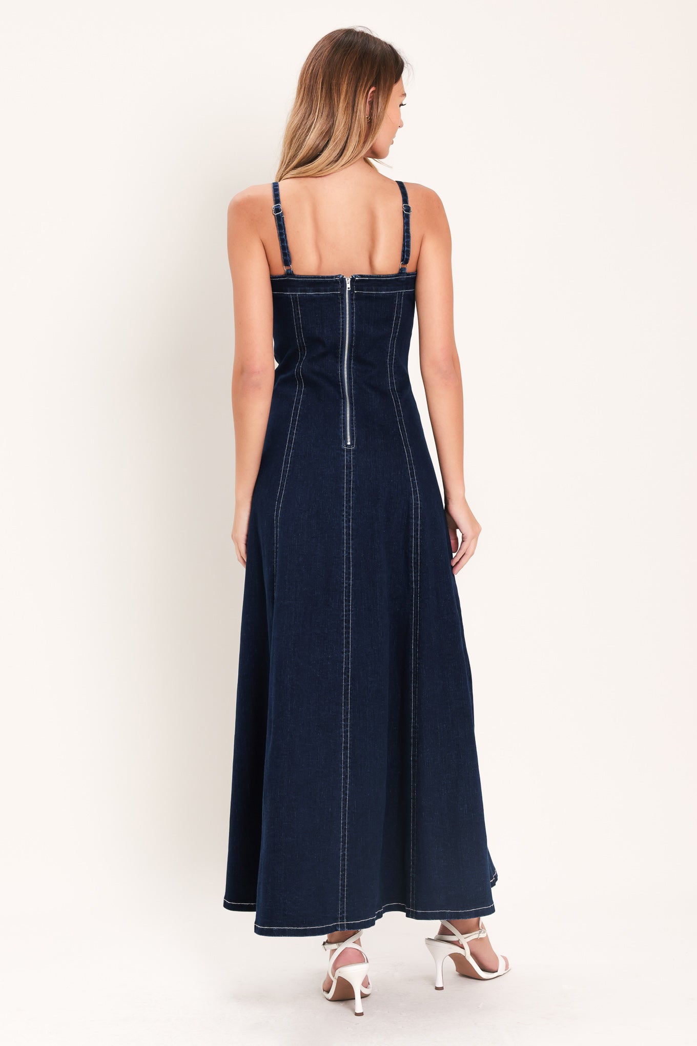 Woman wearing a dark indigo denim midi dress featuring straight neckline with V cut out, straps, circle skirt and back zipper closure | Flying Tomato