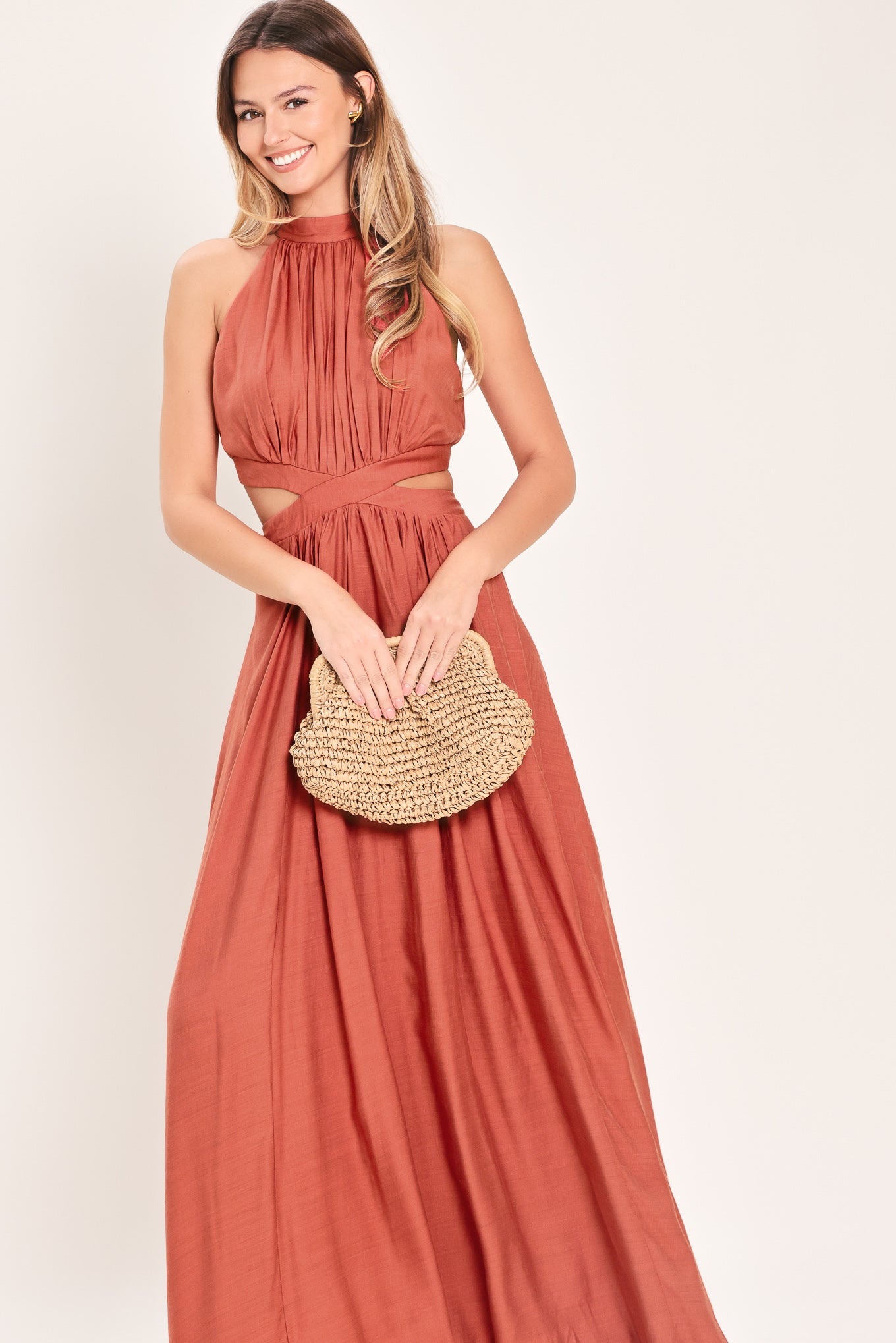 Woman wearing a terracotta maxi dress featuring halter neckline, side cut out and back button/zipper closure | Flying Tomato