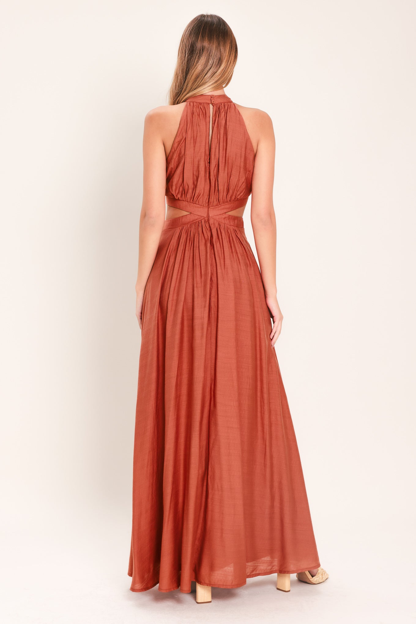 Woman wearing a terracotta maxi dress featuring halter neckline, side cut out and back button/zipper closure | Flying Tomato