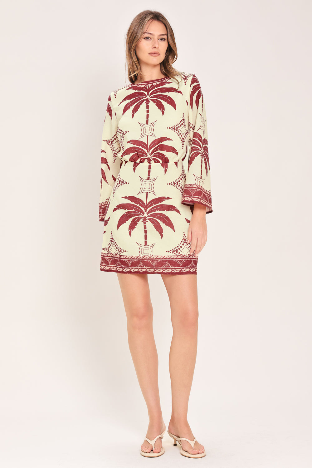 Woman wearing an ivory long sleeve mini dress with maroon palm tree design | Flying Tomato