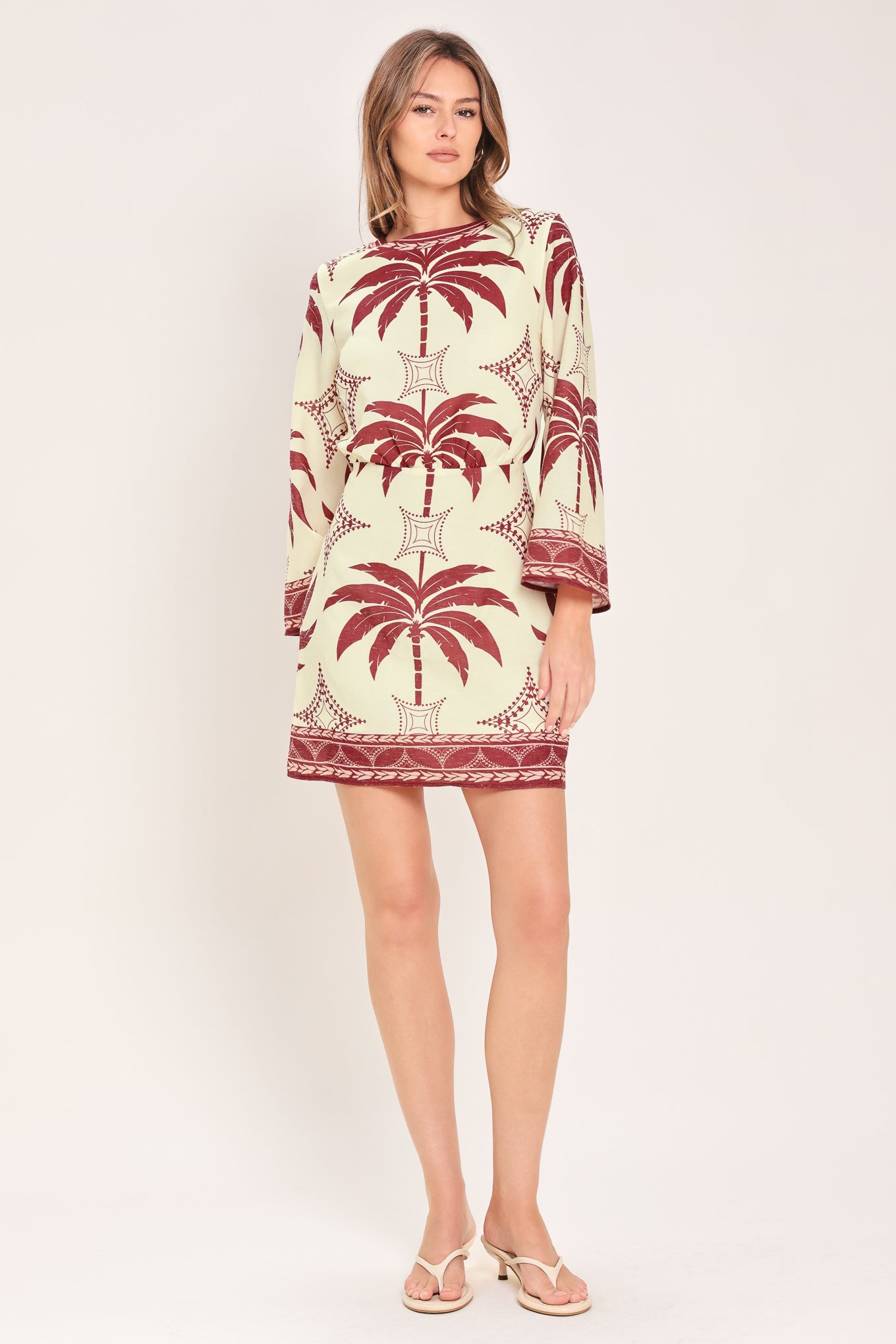 Woman wearing an ivory long sleeve mini dress with maroon palm tree design | Flying Tomato