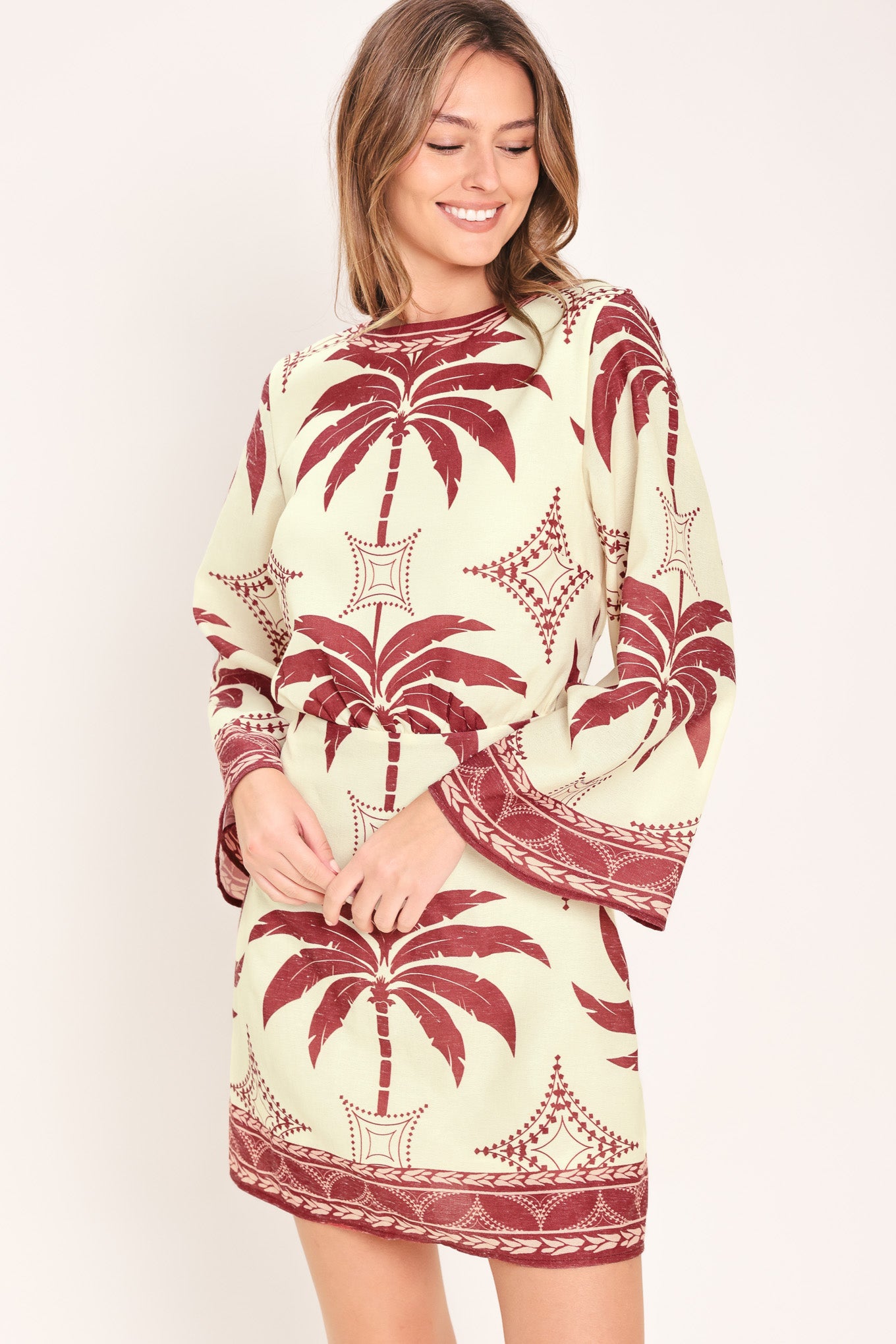 Woman wearing an ivory long sleeve mini dress with maroon palm tree design | Flying Tomato