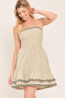 Woman wearing a stone beige strapless mini dress featuring double ruffle hem with embroidered edge and smocked back bodice | Flying Tomato