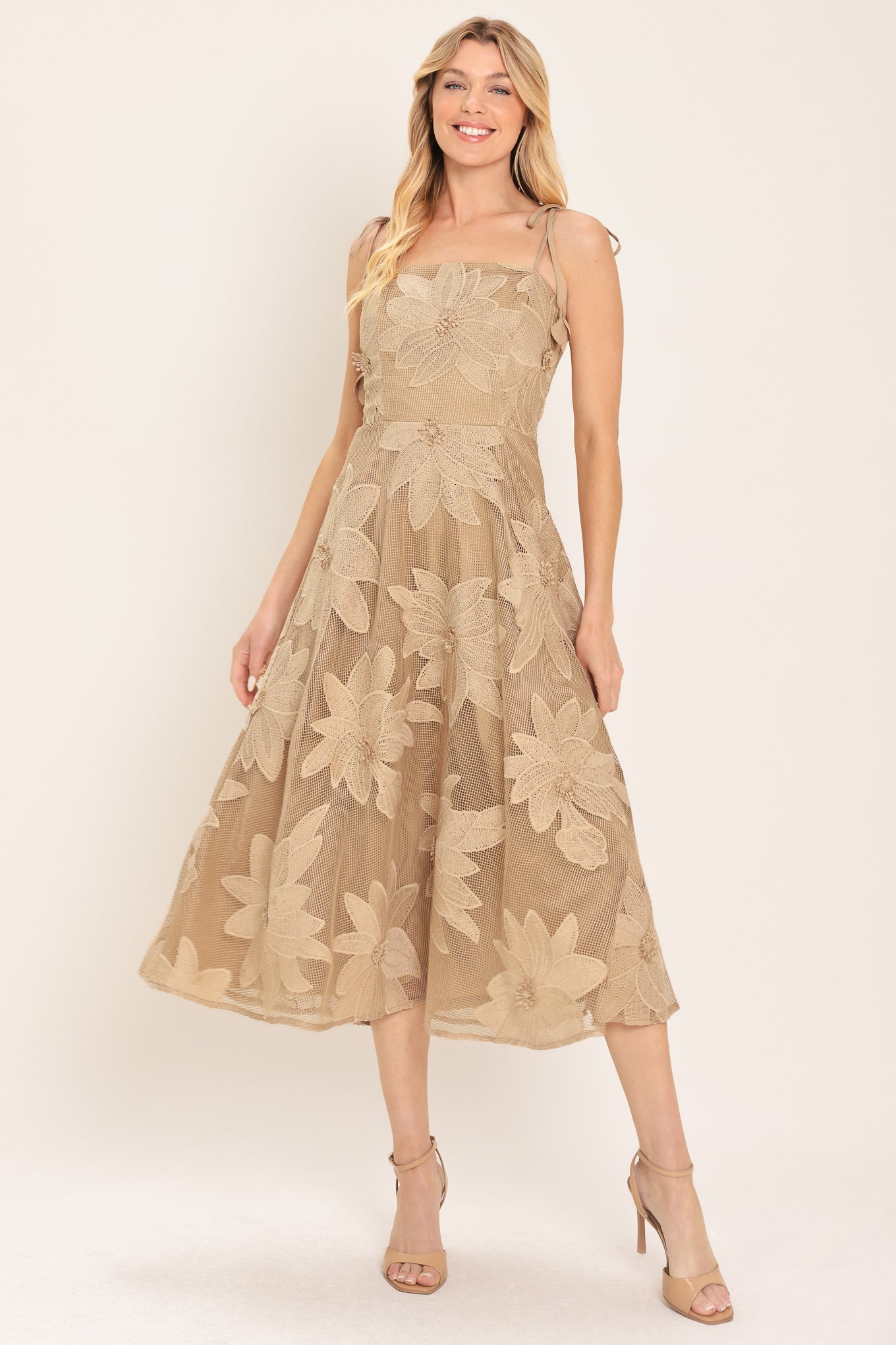 A woman wearing a sleeveless midi dress with a sheer beige mesh base and large floral applique in a matching tan/beige tone, | Flying Tomato