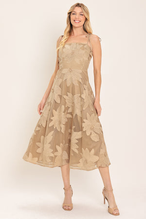A woman wearing a sleeveless midi dress with a sheer beige mesh base and large floral applique in a matching tan/beige tone, | Flying Tomato