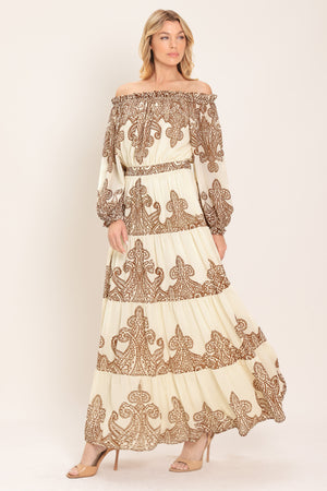 Woman wearing an off-shoulder maxi dress with intricate brown embroidery featuring a smocked back waistband | Flying Tomato