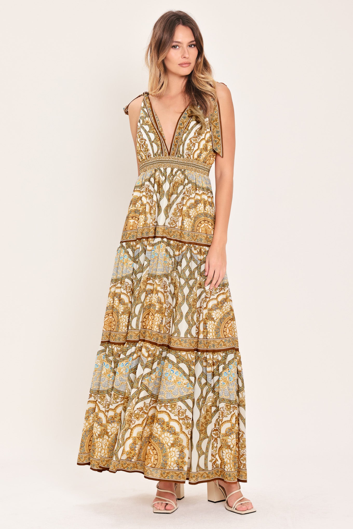 Woman wearing a gold and beige patterned maxi dress featuring front and back V neckline, shoulder ties, smocked waistband and tier skirt | Flying Tomato