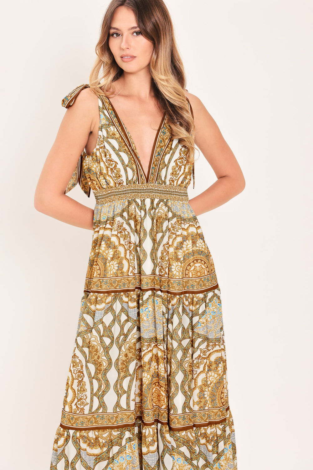 Woman wearing a gold and beige patterned maxi dress featuring front and back V neckline, shoulder ties, smocked waistband and tier skirt | Flying Tomato