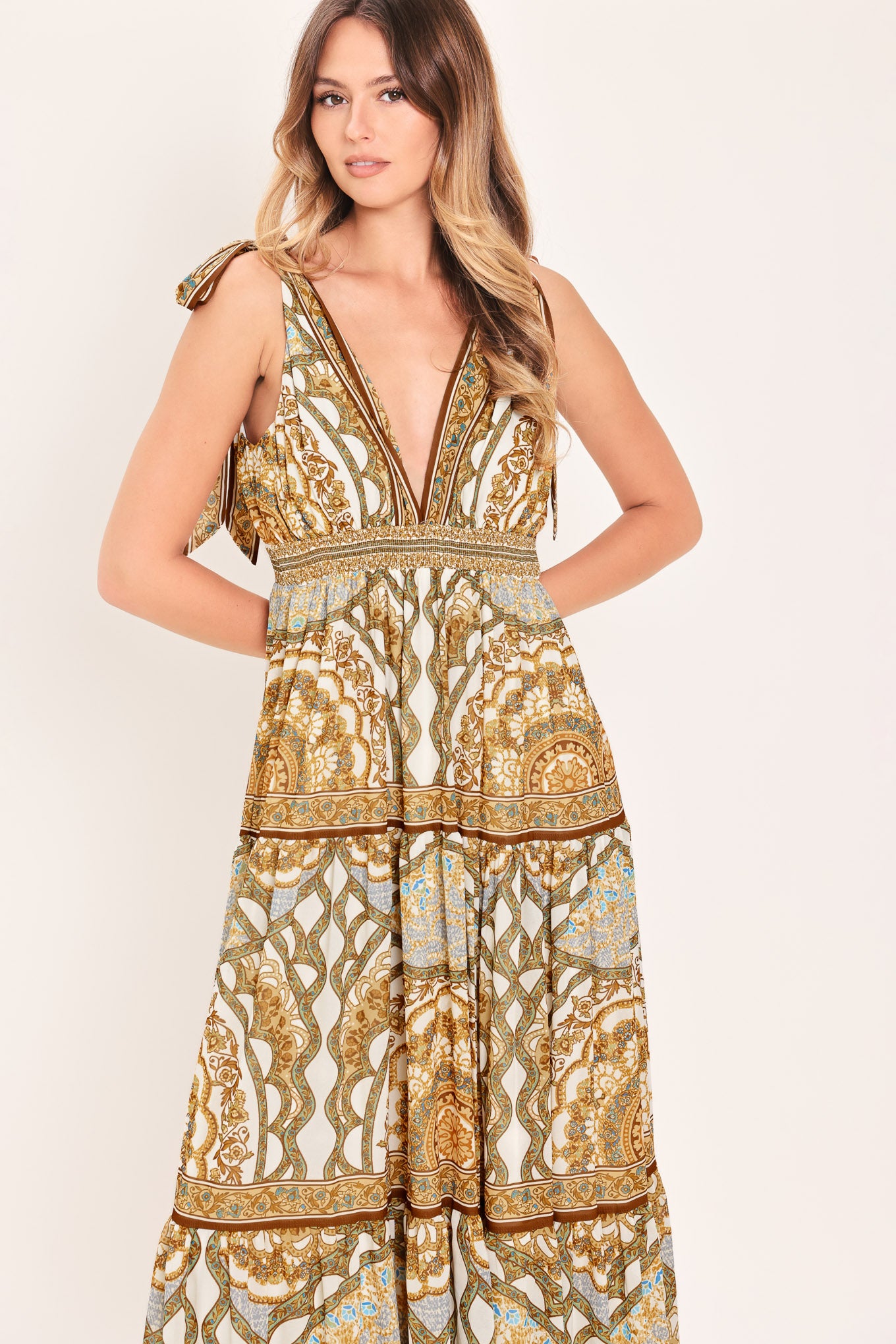 Woman wearing a gold and beige patterned maxi dress featuring front and back V neckline, shoulder ties, smocked waistband and tier skirt | Flying Tomato