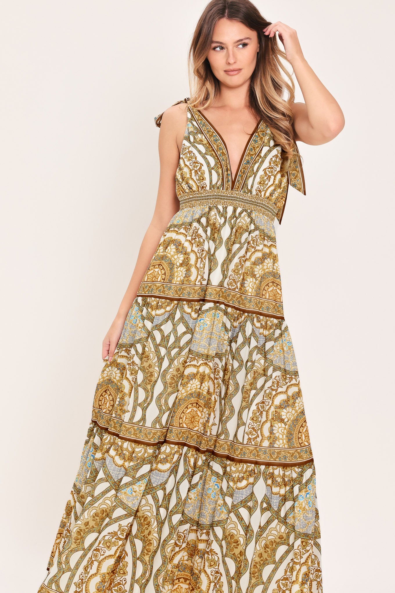 Woman wearing a gold and beige patterned maxi dress featuring front and back V neckline, shoulder ties, smocked waistband and tier skirt | Flying Tomato
