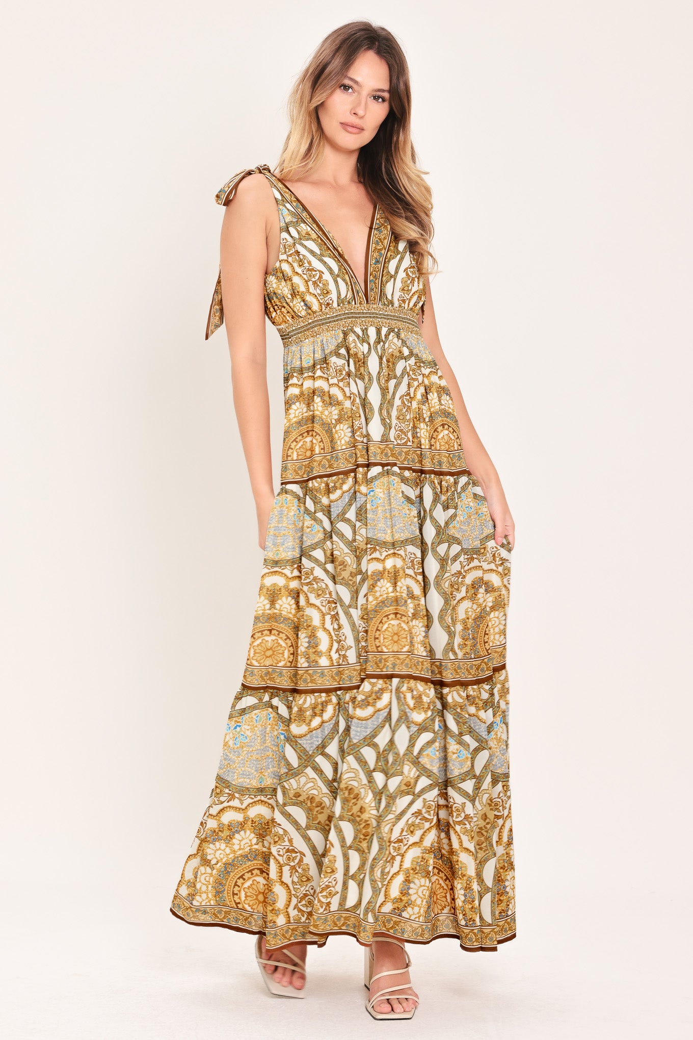 Woman wearing a gold and beige patterned maxi dress featuring front and back V neckline, shoulder ties, smocked waistband and tier skirt | Flying Tomato