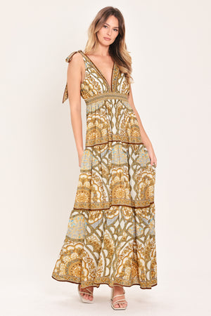 Woman wearing a gold and beige patterned maxi dress featuring front and back V neckline, shoulder ties, smocked waistband and tier skirt | Flying Tomato