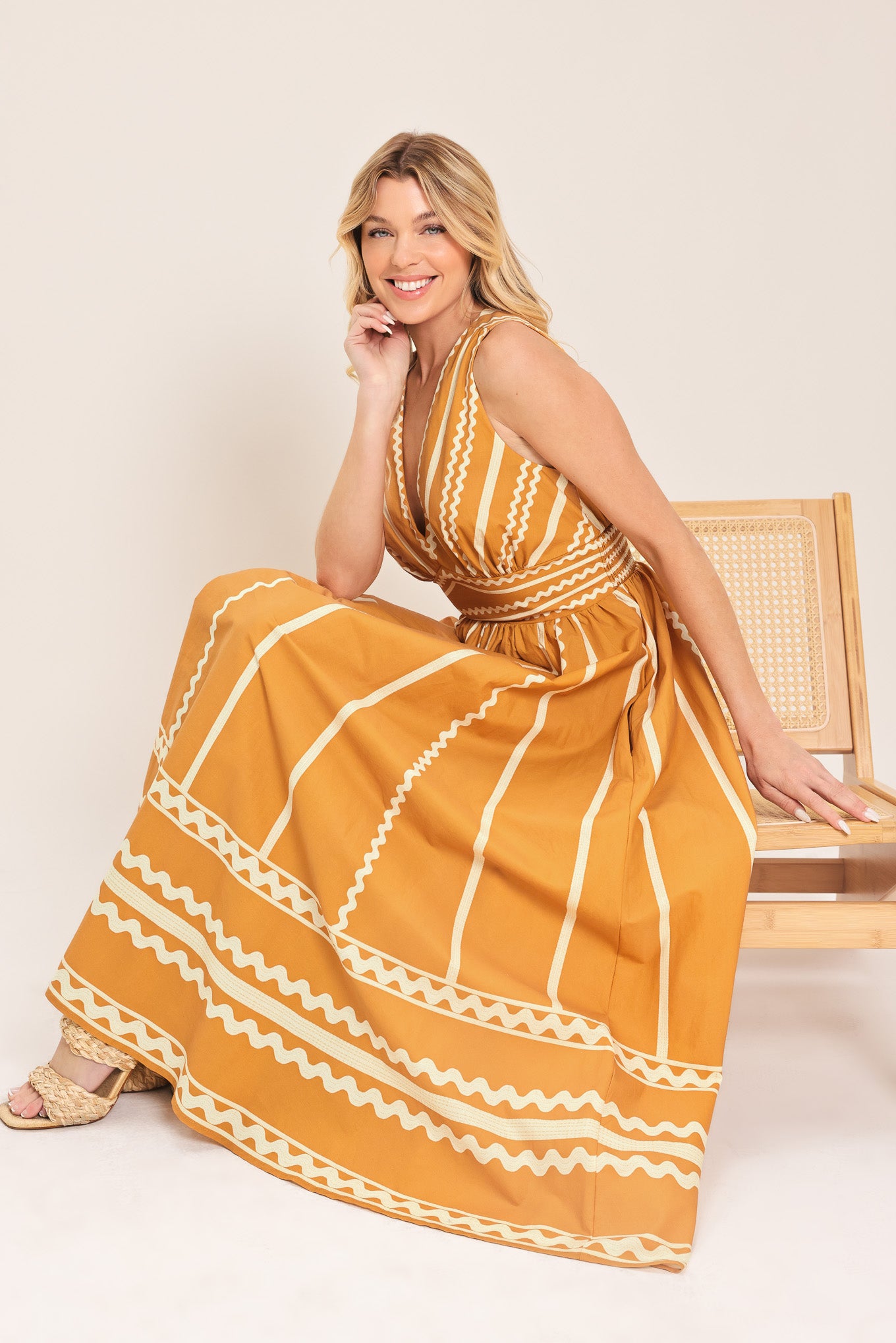 Woman wearing a mustard yellow midi dress with white patterns featuring V neckline, sleeveless, waist yoke, full skirt and smocked back waistband | Flying Tomato