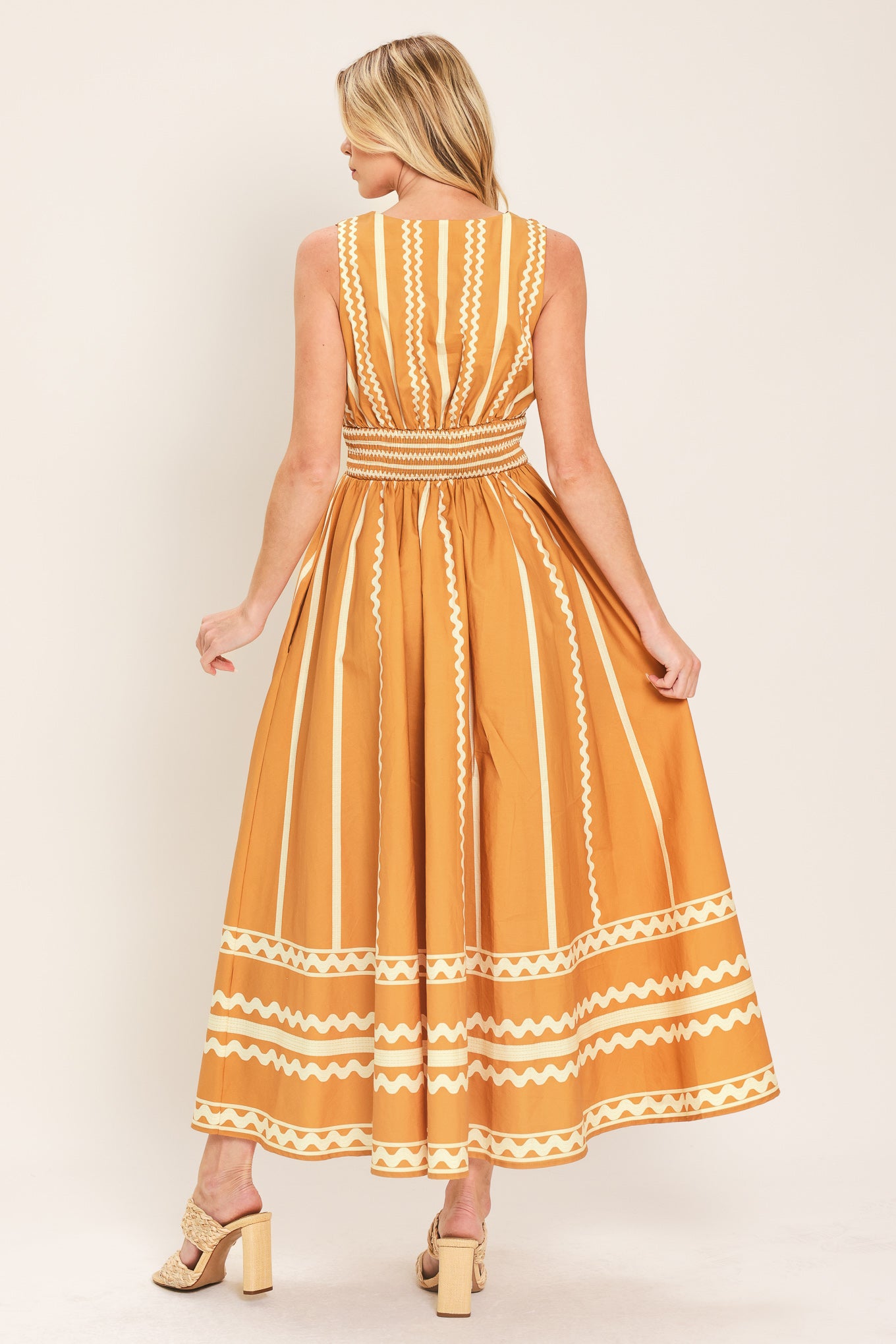 Woman wearing a mustard yellow midi dress with white patterns featuring V neckline, sleeveless, waist yoke, full skirt and smocked back waistband | Flying Tomato
