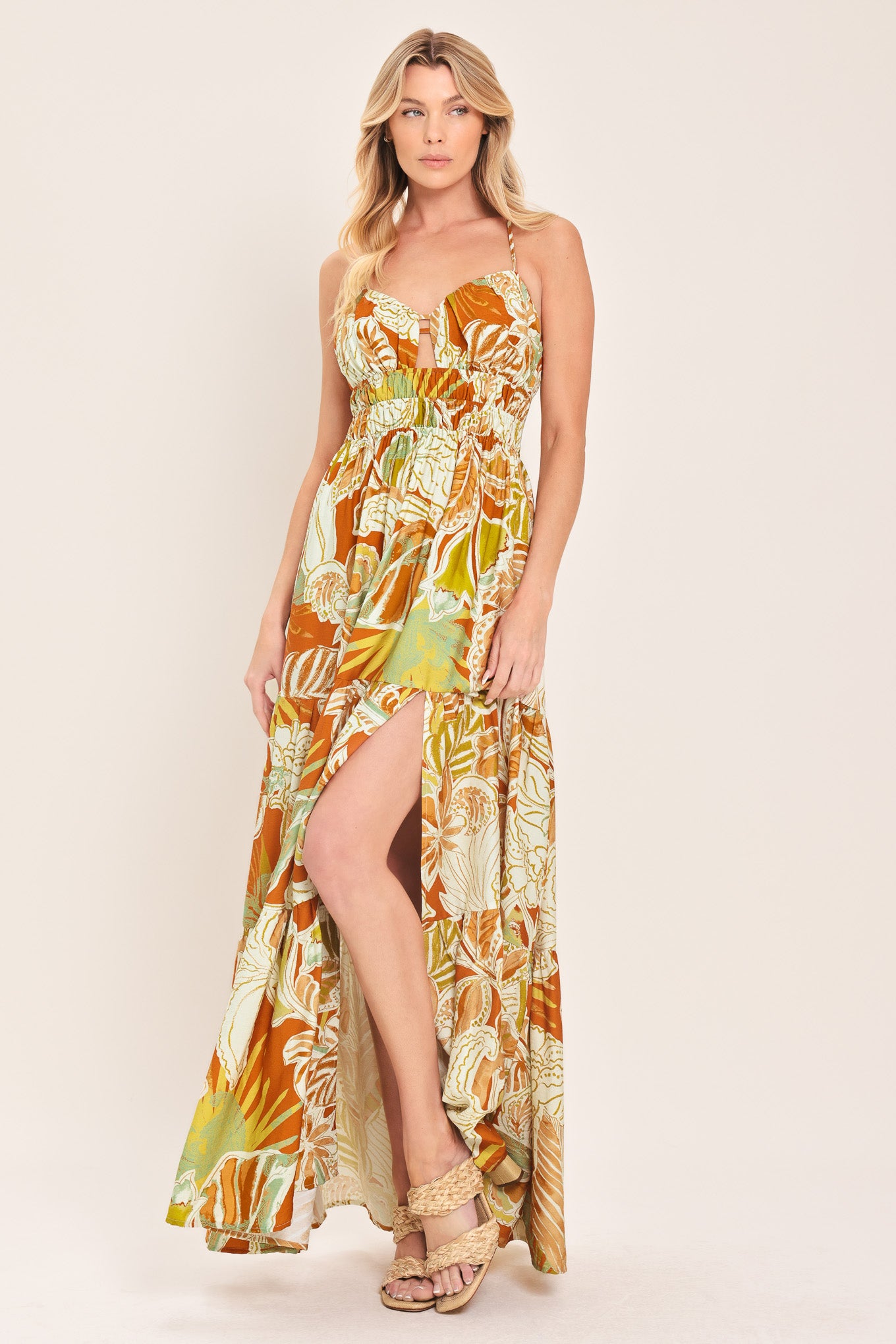 Woman wearing a colorful tropical floral maxi dress featuring cami top, wide smocked waist, slit tier skirt and bare back with cross straps | Flying Tomato