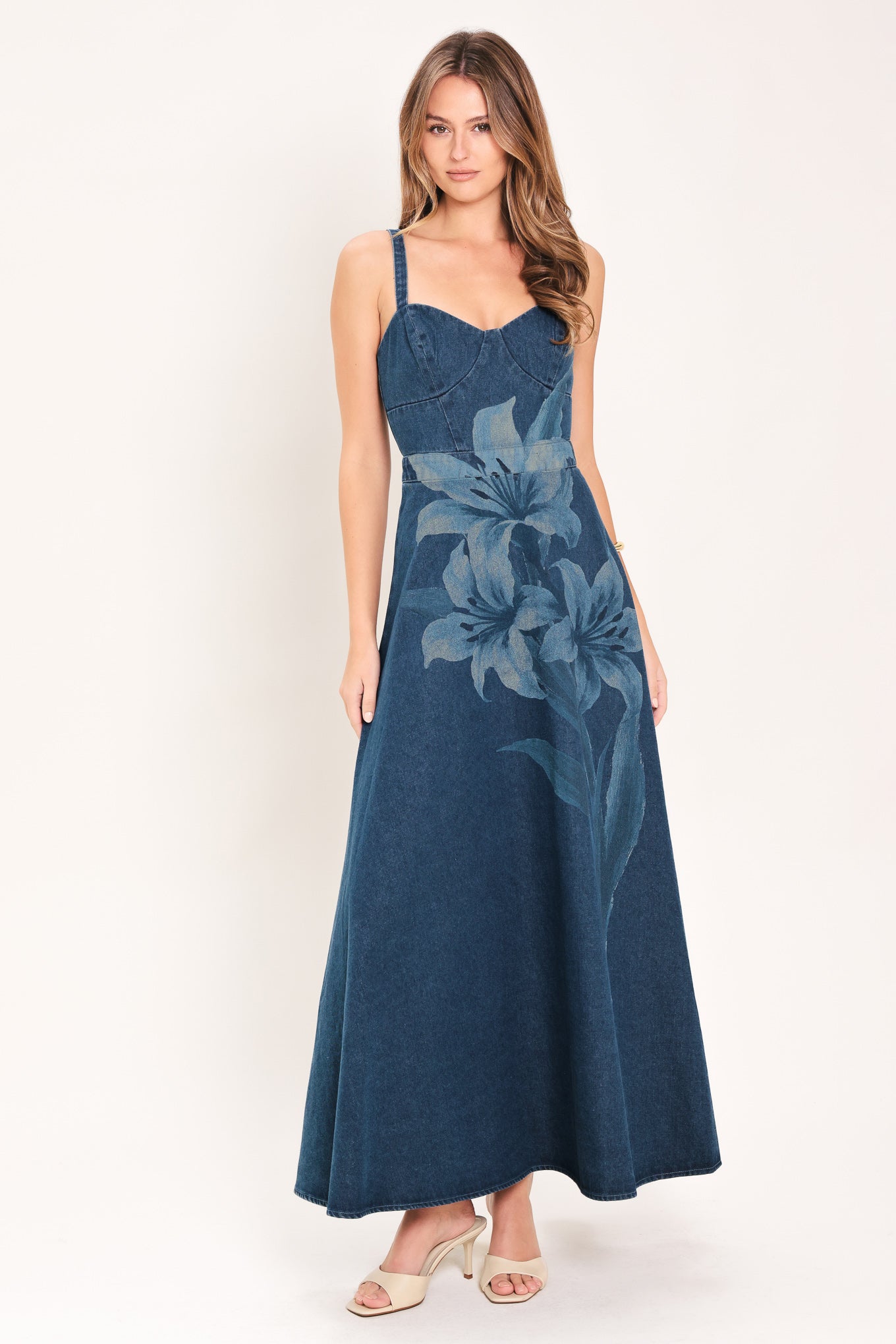 Woman wearing a blue denim midi dress with lilies printed featuring bustier top, straps, circle skirt and back zipper closure | Flying Tomato