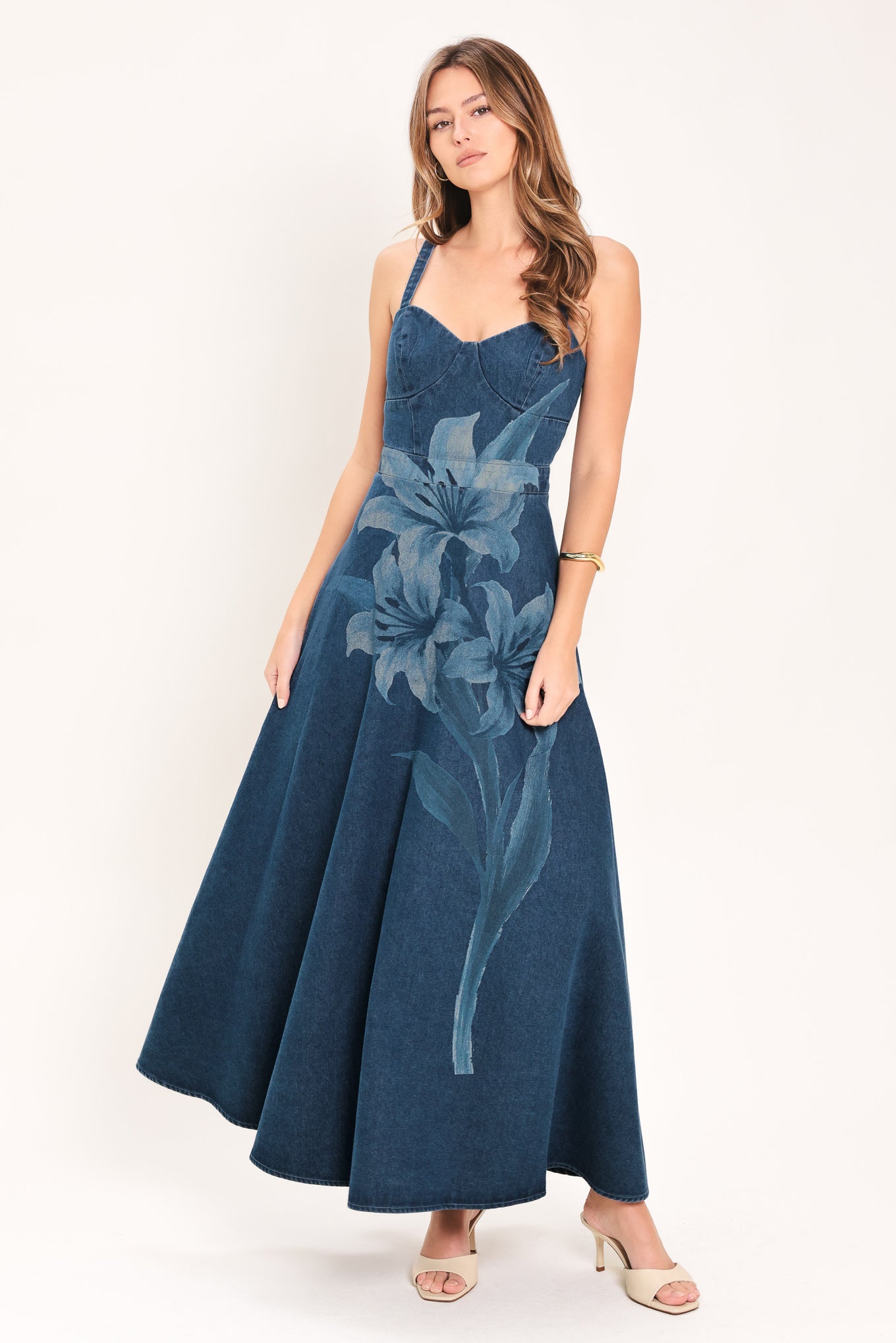 Woman wearing a blue denim midi dress with lilies printed featuring bustier top, straps, circle skirt and back zipper closure | Flying Tomato