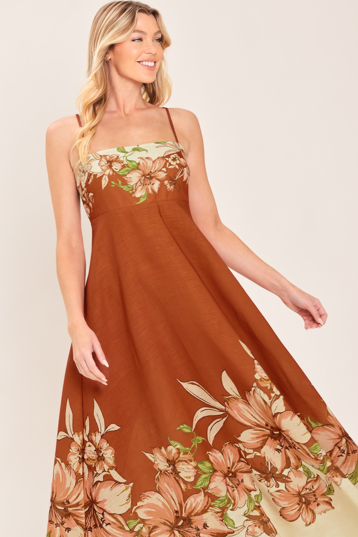 Woman wearing a terracotta midi dress with floral print on the top and bottom, featuring straight neckline, straps, circle skirt and back zipper closure | Flying Tomato