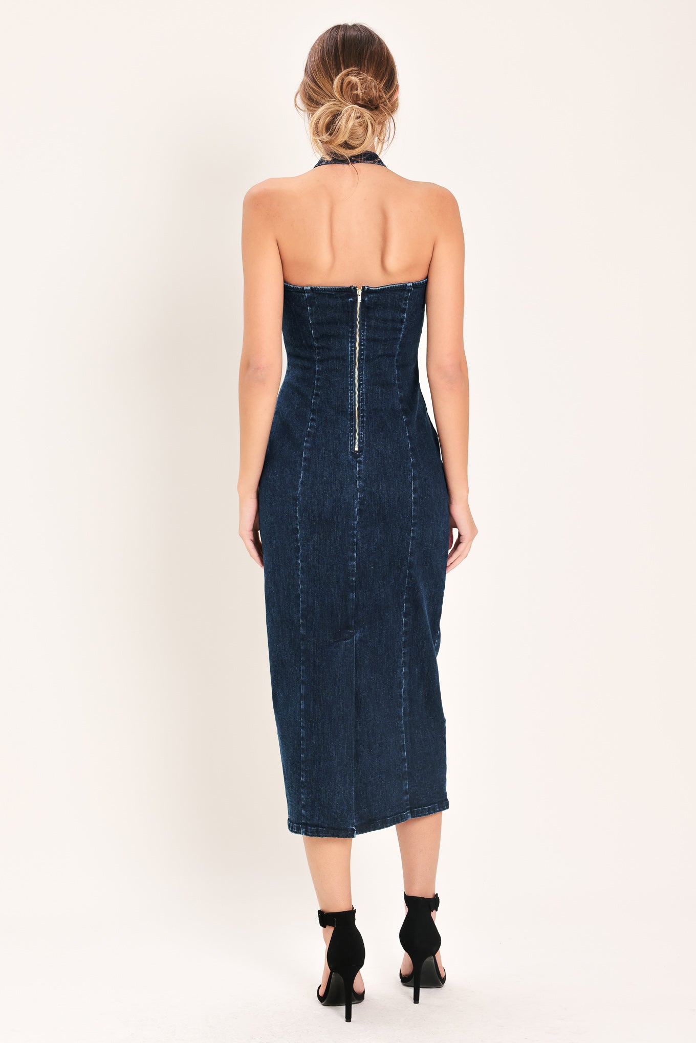 Woman wearing a dark indigo denim midi dress featuring halter neckline with hardware, bare back and zipper closure | Flying Tomato