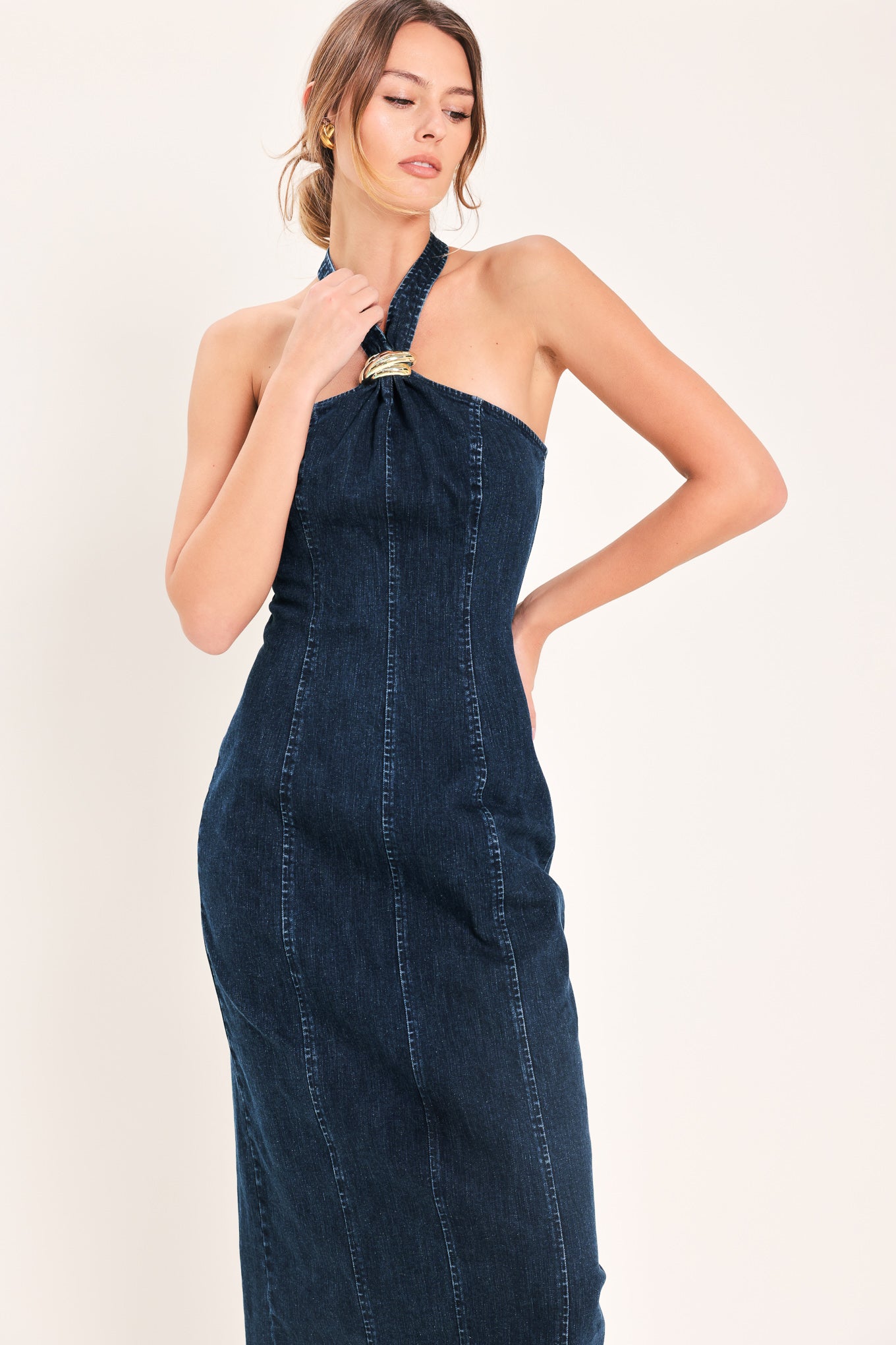 Woman wearing a dark indigo denim midi dress featuring halter neckline with hardware, bare back and zipper closure | Flying Tomato