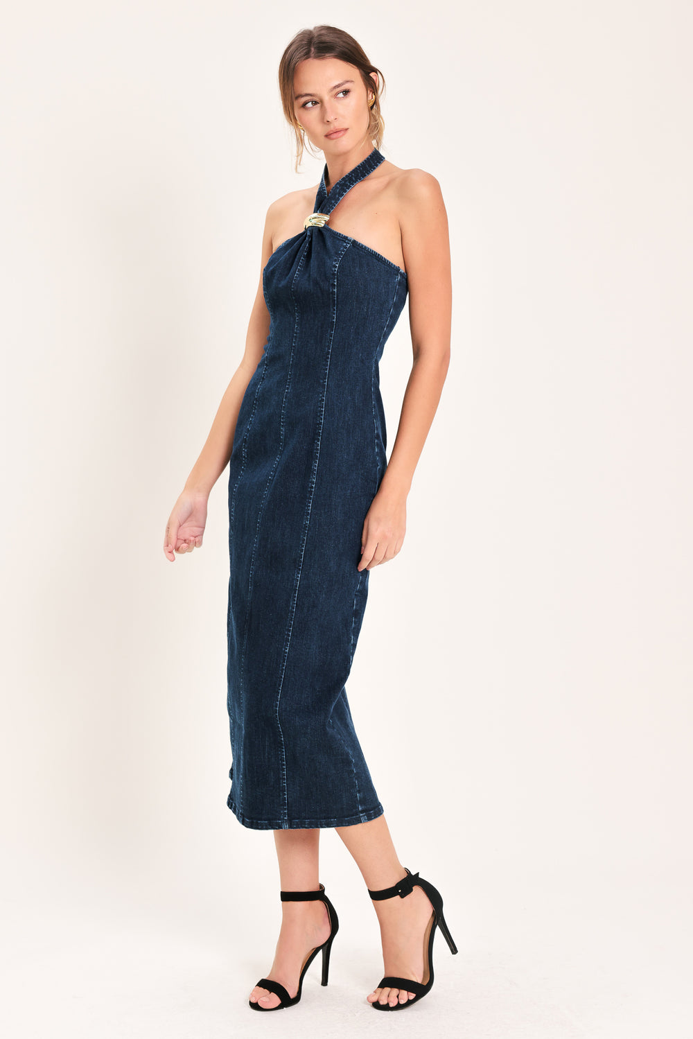 Woman wearing a dark indigo denim midi dress featuring halter neckline with hardware, bare back and zipper closure | Flying Tomato