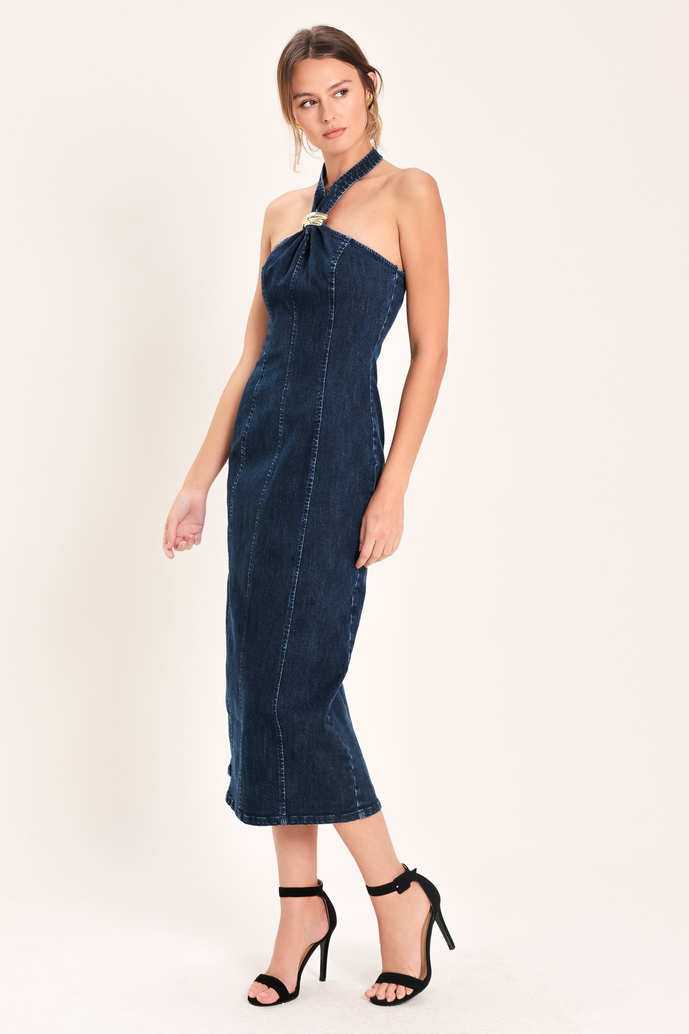 Woman wearing a dark indigo denim midi dress featuring halter neckline with hardware, bare back and zipper closure | Flying Tomato