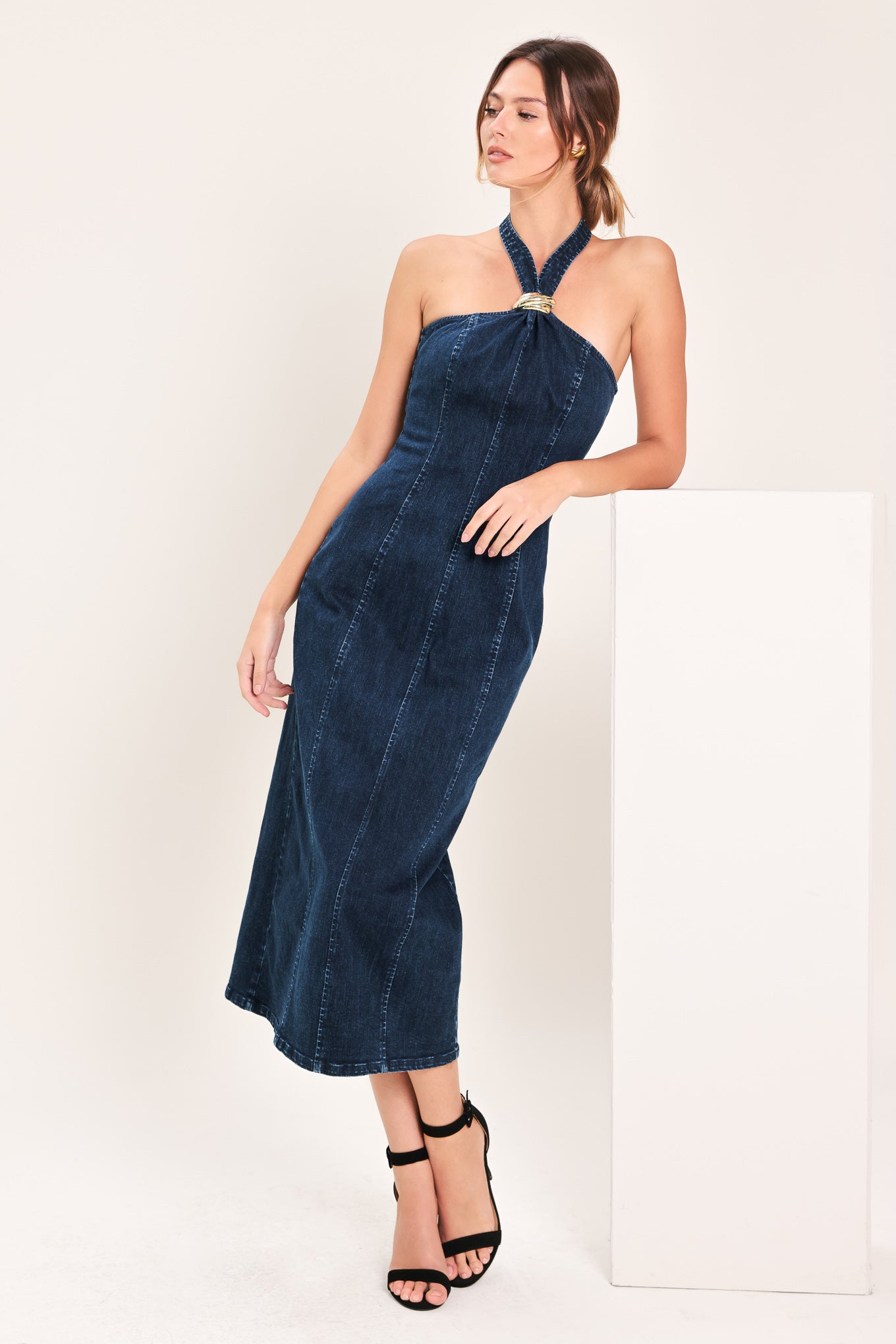 Woman wearing a dark indigo denim midi dress featuring halter neckline with hardware, bare back and zipper closure | Flying Tomato