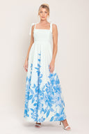 Woman wearing a white maxi dress with blue floral pattern featuring straight neckline, shoulder ties, full skirt and smocked back bodice | Flying Tomato