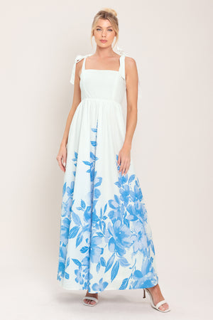 Woman wearing a white maxi dress with blue floral pattern featuring straight neckline, shoulder ties, full skirt and smocked back bodice | Flying Tomato
