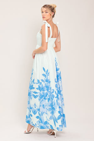 Woman wearing a white maxi dress with blue floral pattern featuring straight neckline, shoulder ties, full skirt and smocked back bodice | Flying Tomato