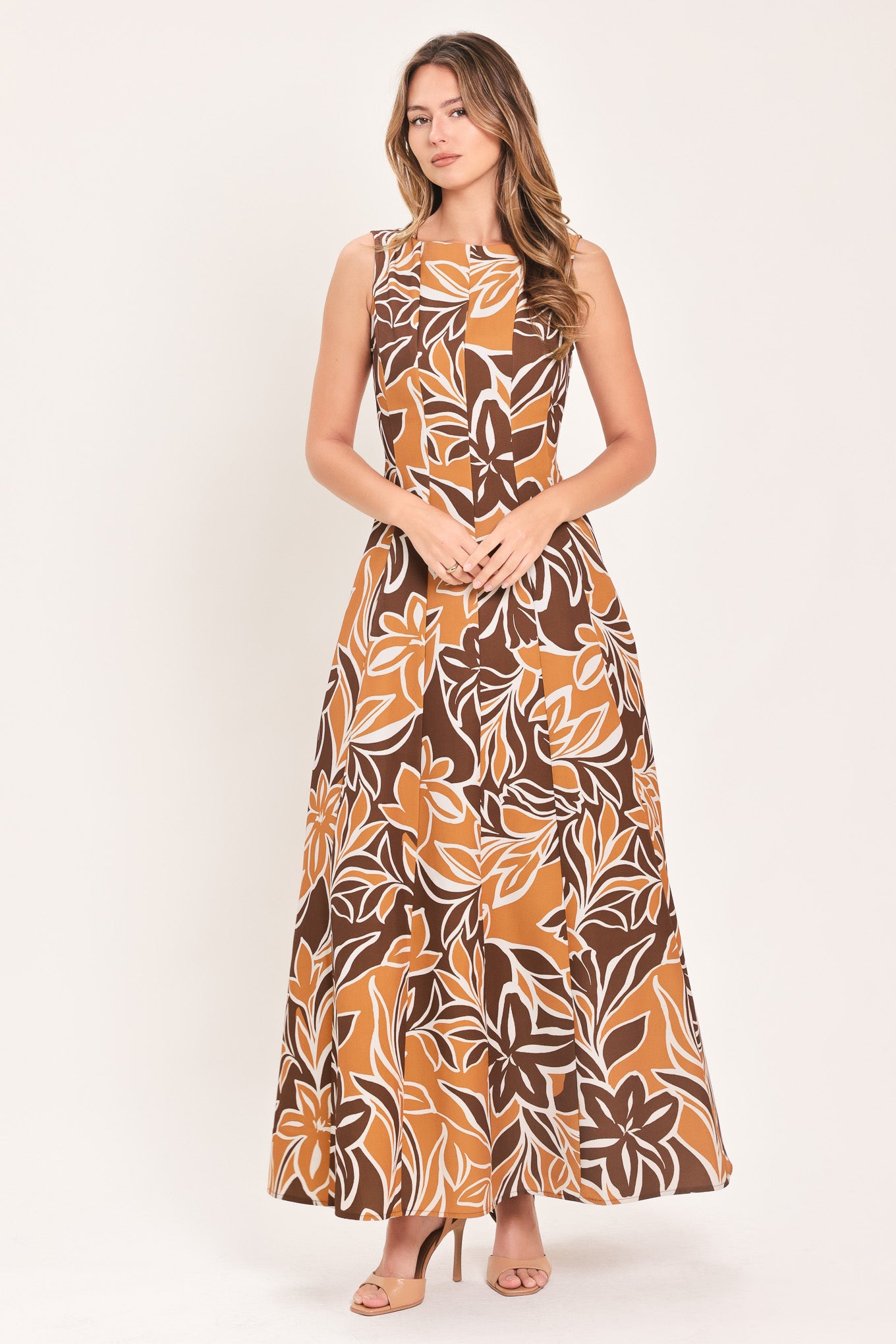 A woman modeling a sleeveless, floor-length maxi dress with a bold brown, tan, and white tropical floral pattern | Flying Tomato