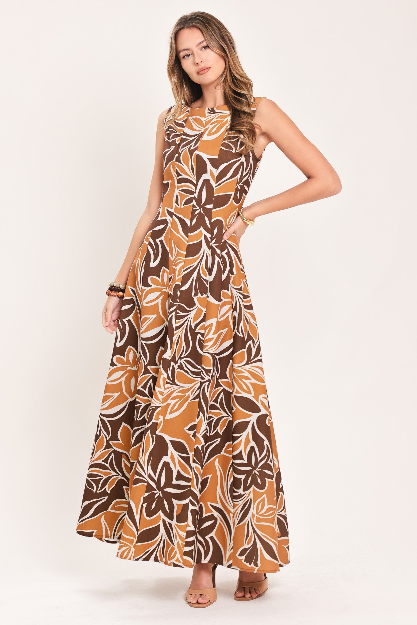 A woman modeling a sleeveless, floor-length maxi dress with a bold brown, tan, and white tropical floral pattern | Flying Tomato