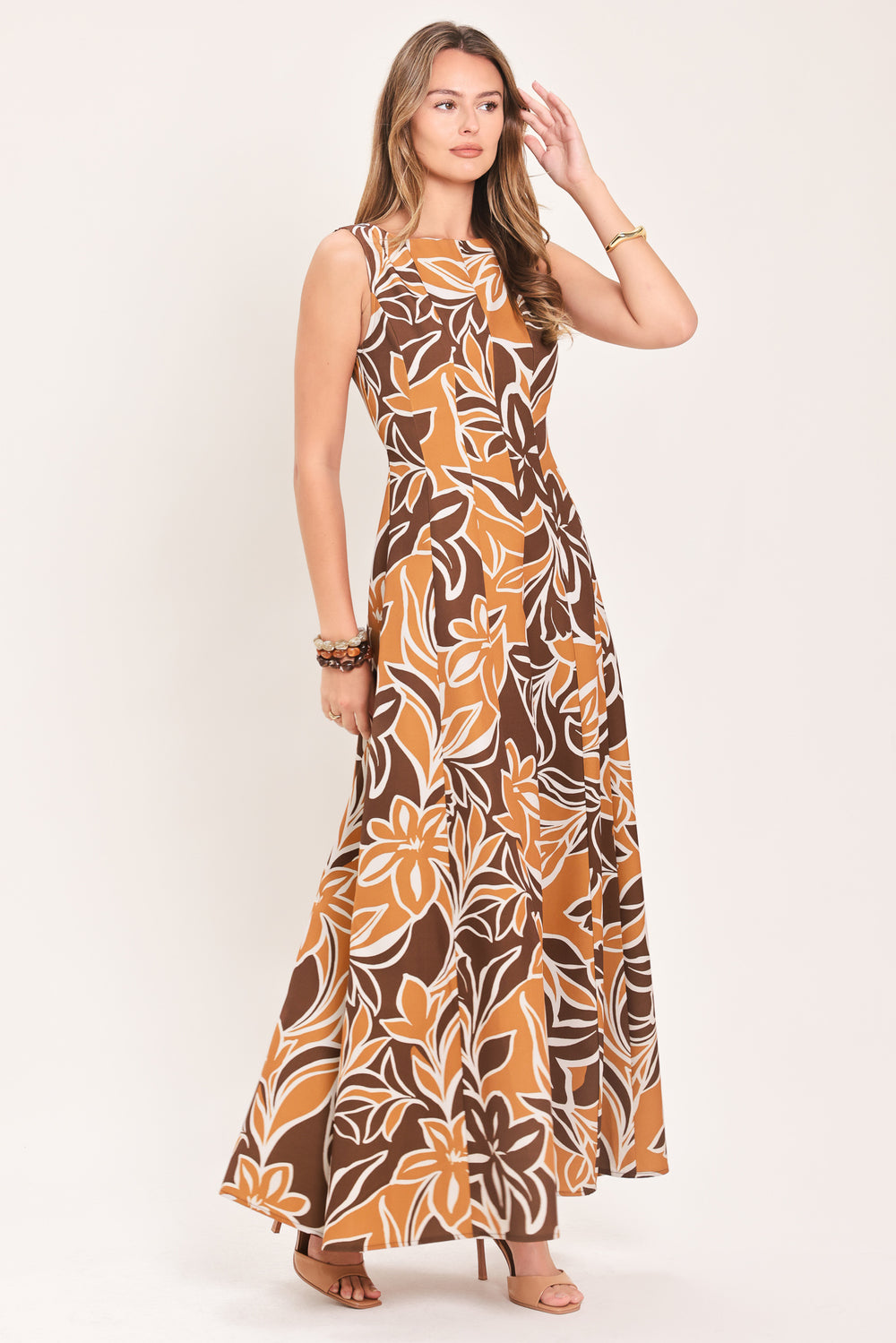 A woman modeling a sleeveless, floor-length maxi dress with a bold brown, tan, and white tropical floral pattern | Flying Tomato