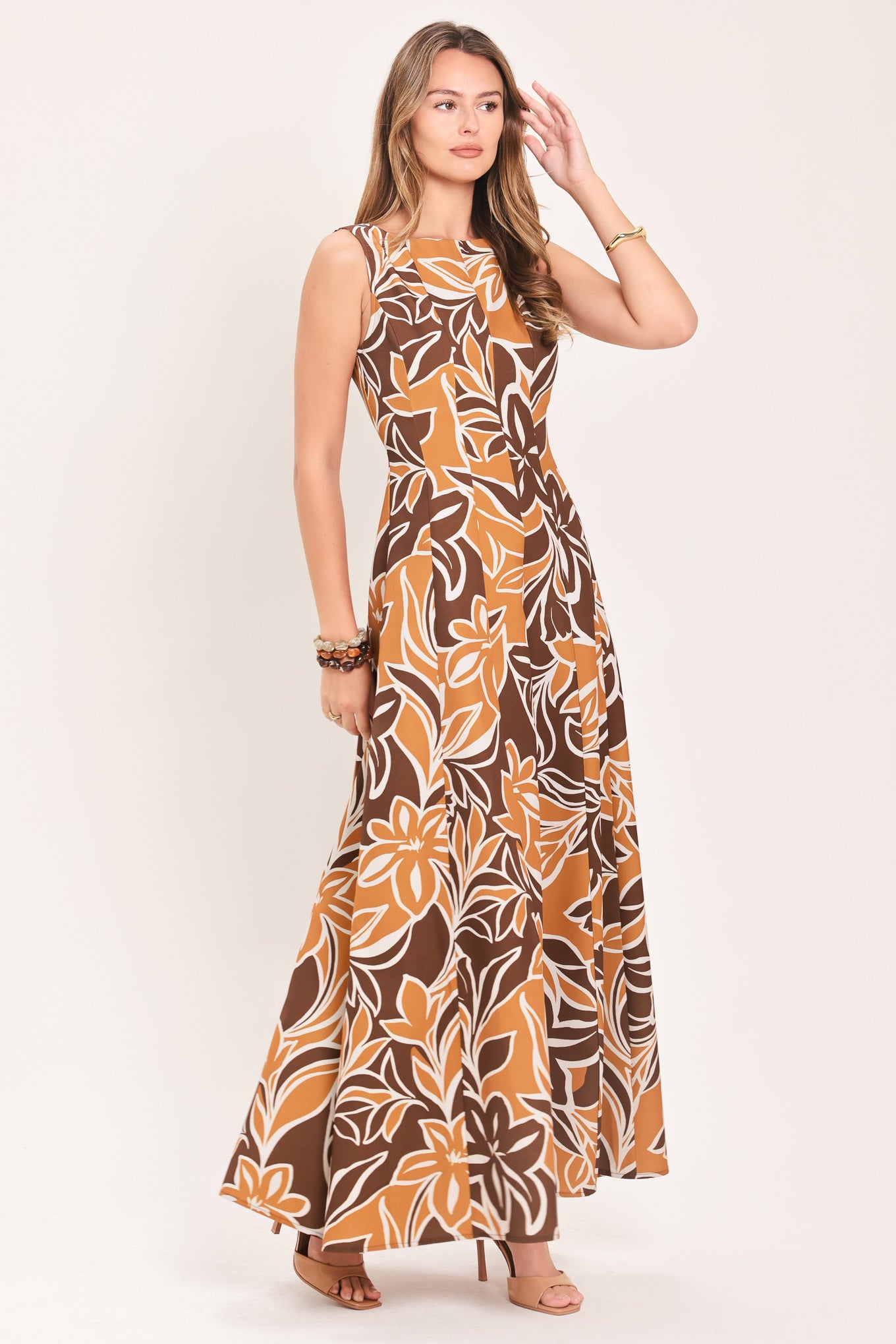 A woman modeling a sleeveless, floor-length maxi dress with a bold brown, tan, and white tropical floral pattern | Flying Tomato