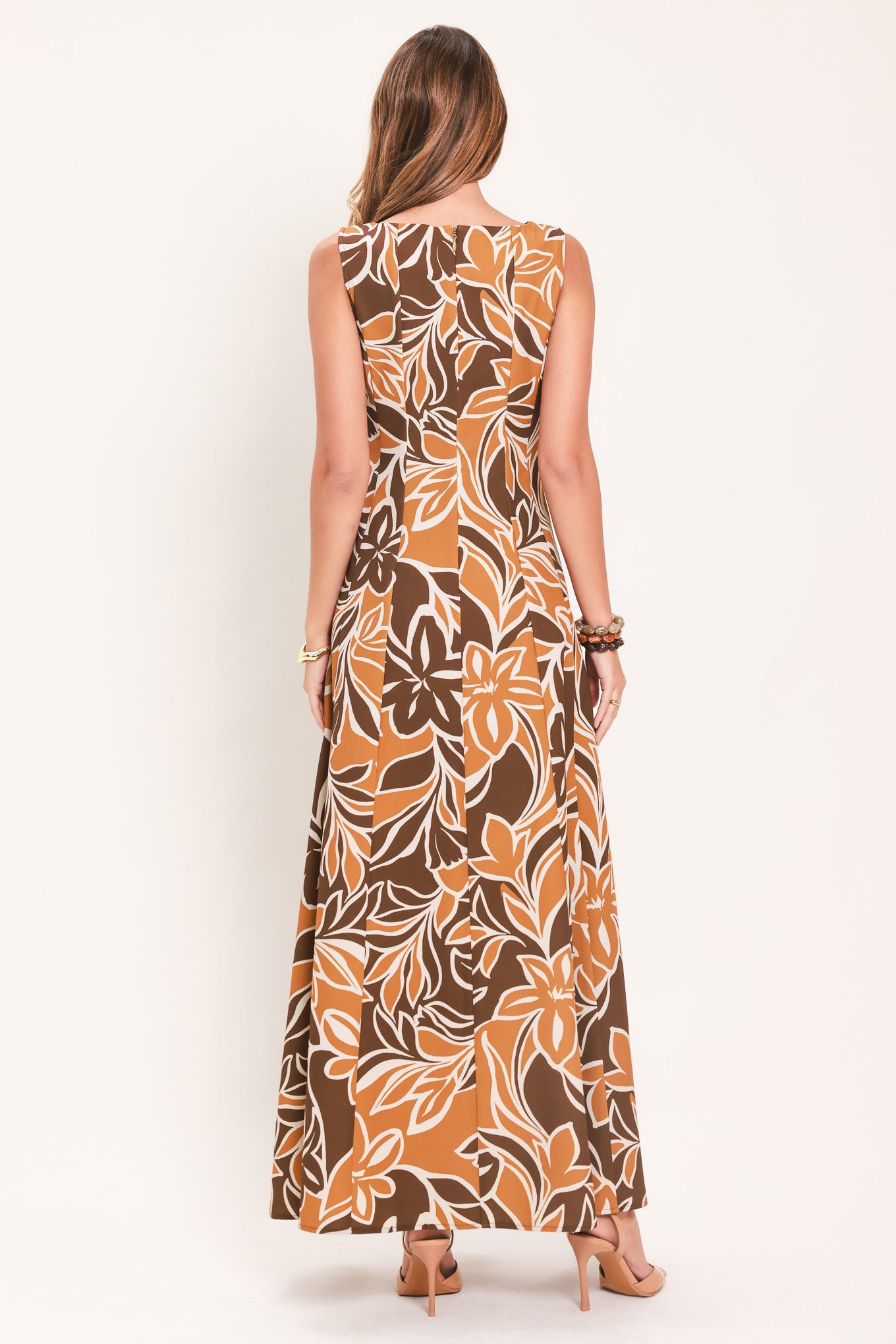 A woman modeling a sleeveless, floor-length maxi dress with a bold brown, tan, and white tropical floral pattern | Flying Tomato