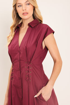 Woman wearing a burgundy midi dress featuring V neckline with collared finish, short sleeve, lace up corset waist and front button down | Flying Tomato