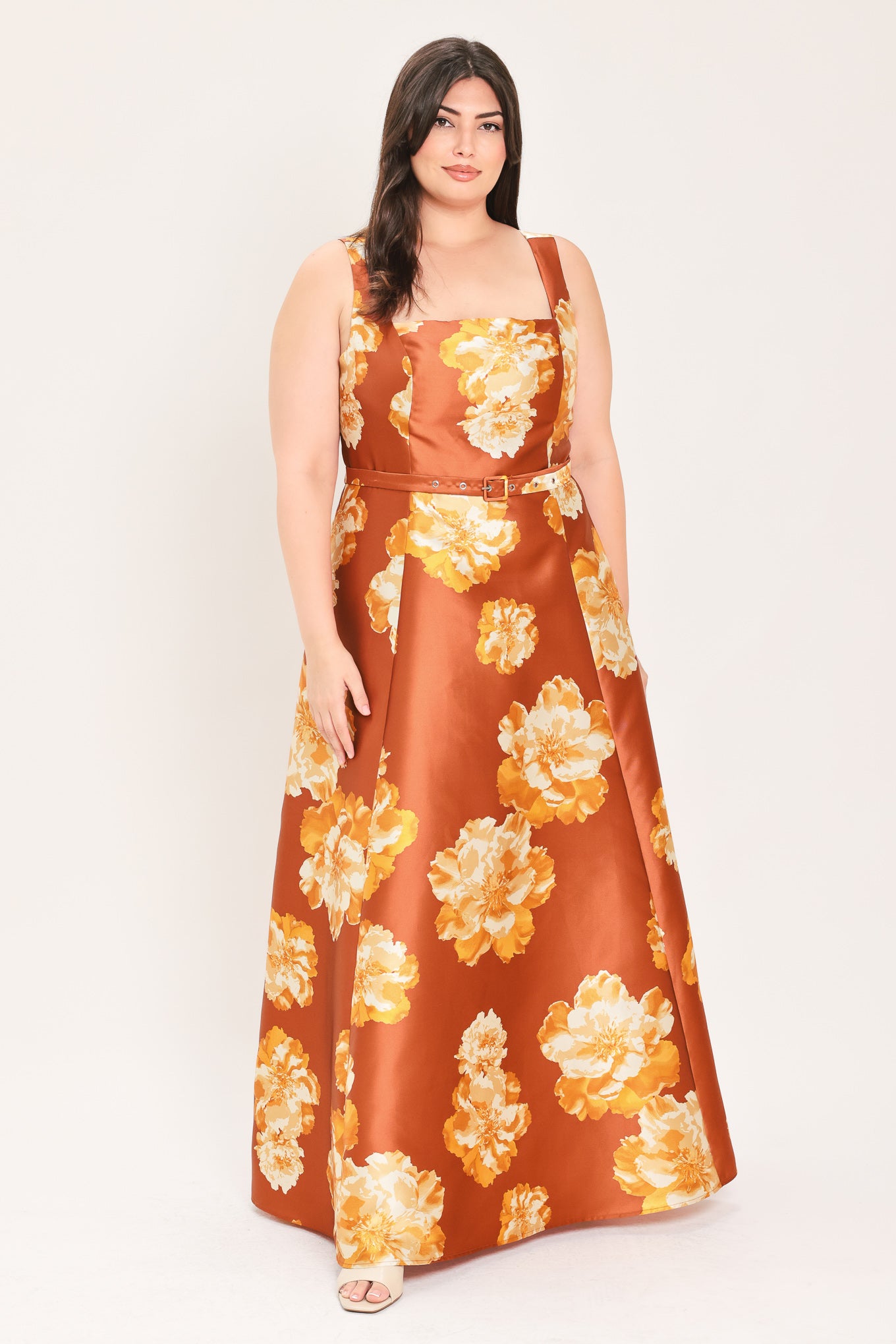 A woman modeling a sleeveless, maxi satin dress in rust orange with a large yellow and white floral print, featuring a matching belt at the waist | Flying Tomato Curve