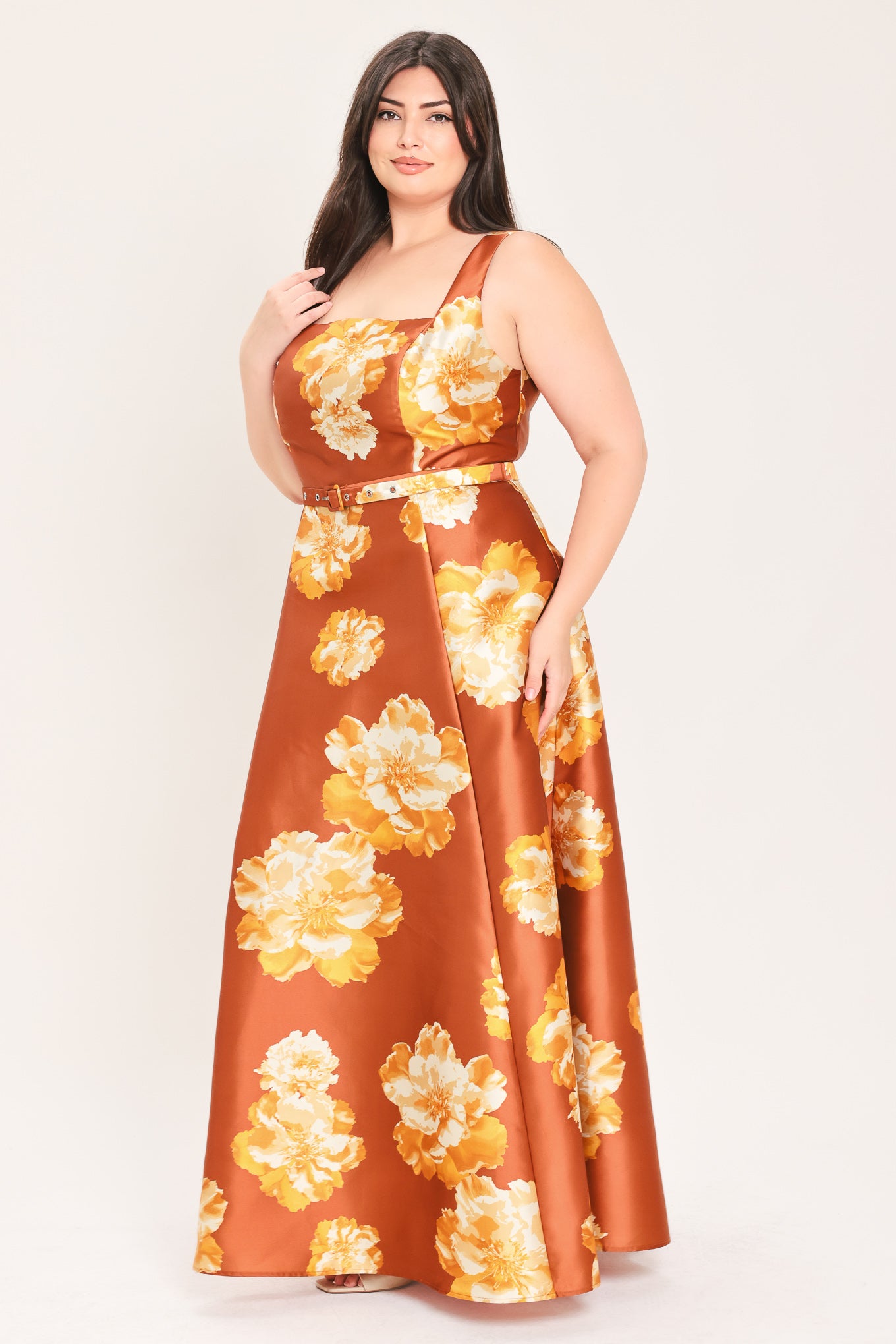 A woman modeling a sleeveless, maxi satin dress in rust orange with a large yellow and white floral print, featuring a matching belt at the waist | Flying Tomato Curve