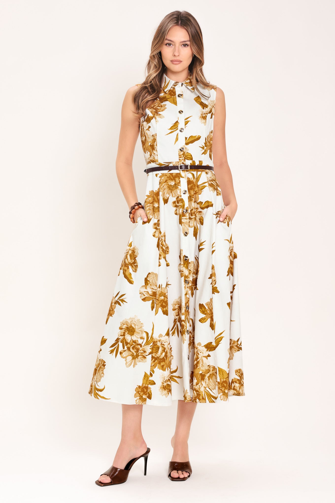Woman wearing a sleeveless ivory midi dress with brown floral print featuring collar, front button down, contrasting belt and circle skirt | Flying Tomato