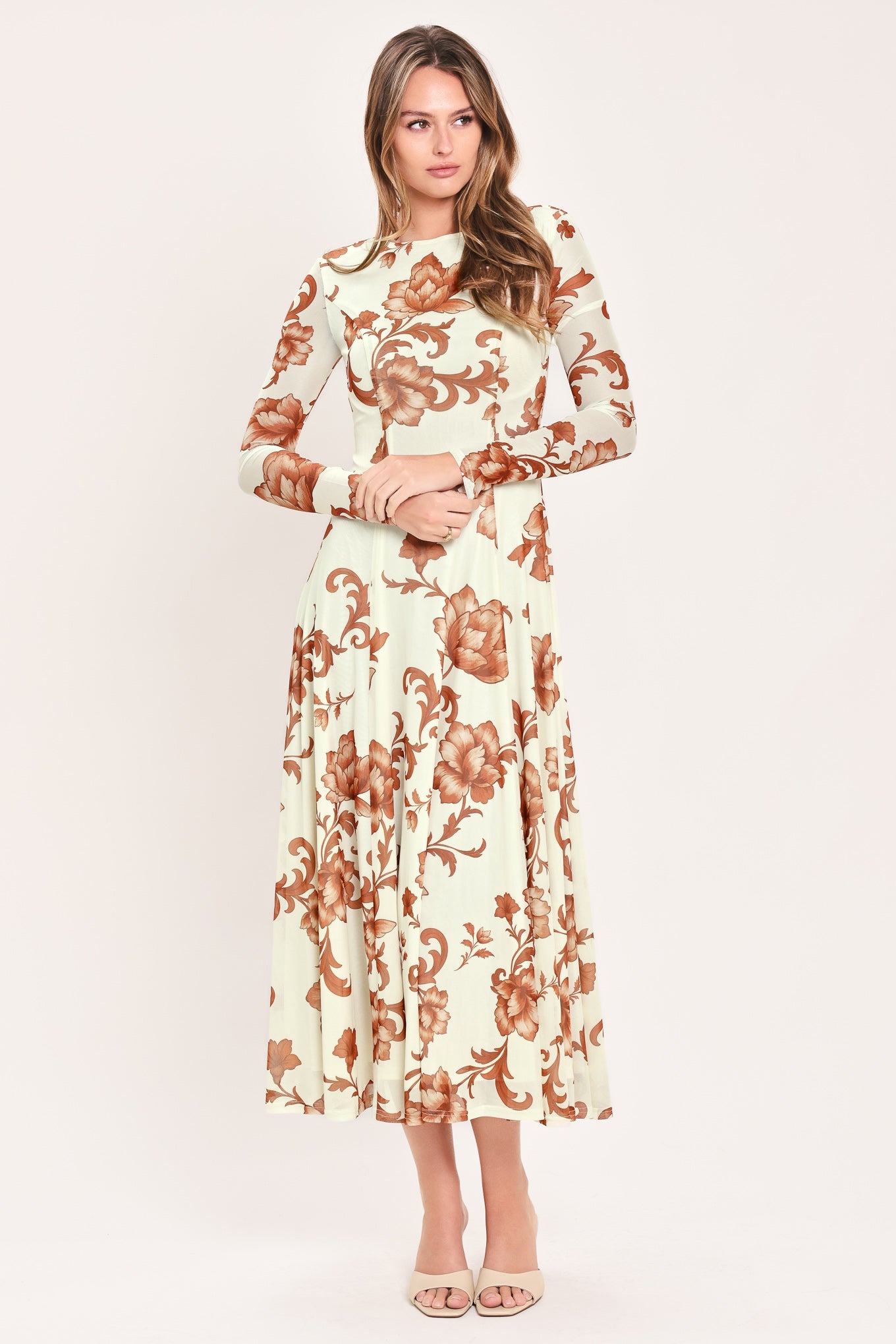 A woman wearing a long-sleeve midi dress with a cream base and a brown baroque-style floral pattern | Flying Tomato