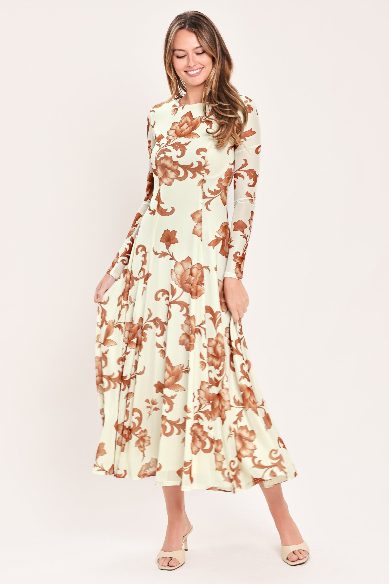 A woman wearing a long-sleeve midi dress with a cream base and a brown baroque-style floral pattern | Flying Tomato